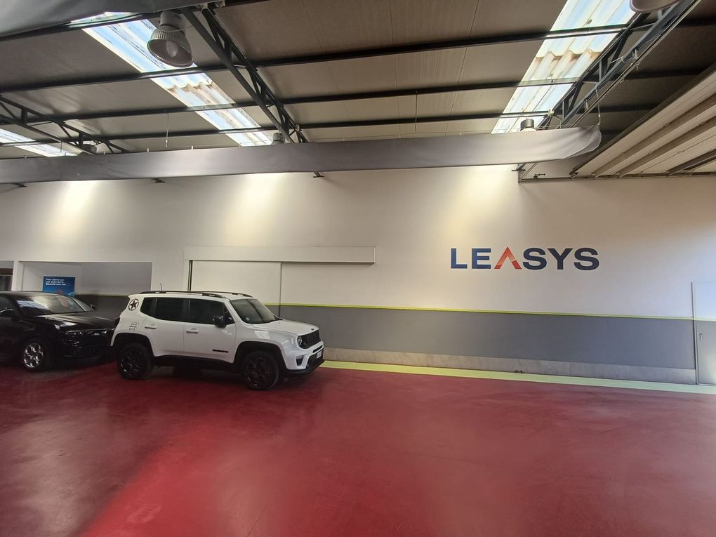 Magazzino al coperto con pavimento rosso, SUV parcheggiati e logo LEASYS sulla parete.