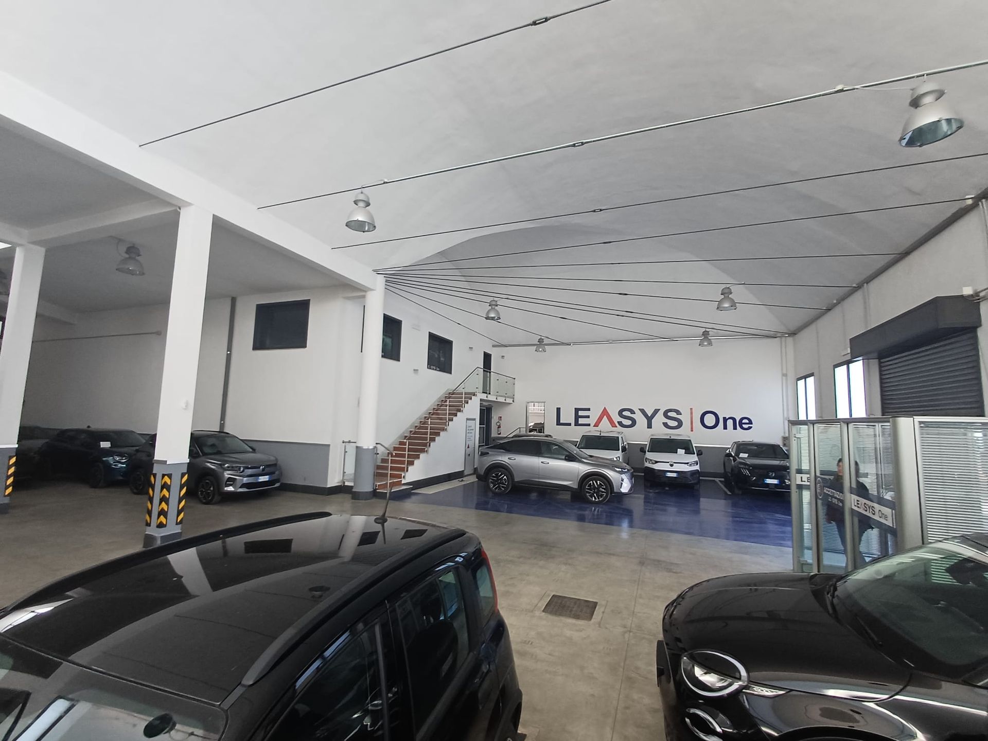 Garage interno con auto parcheggiate, una motocicletta e una macchina per incisione laser sotto un soffitto bianco.
