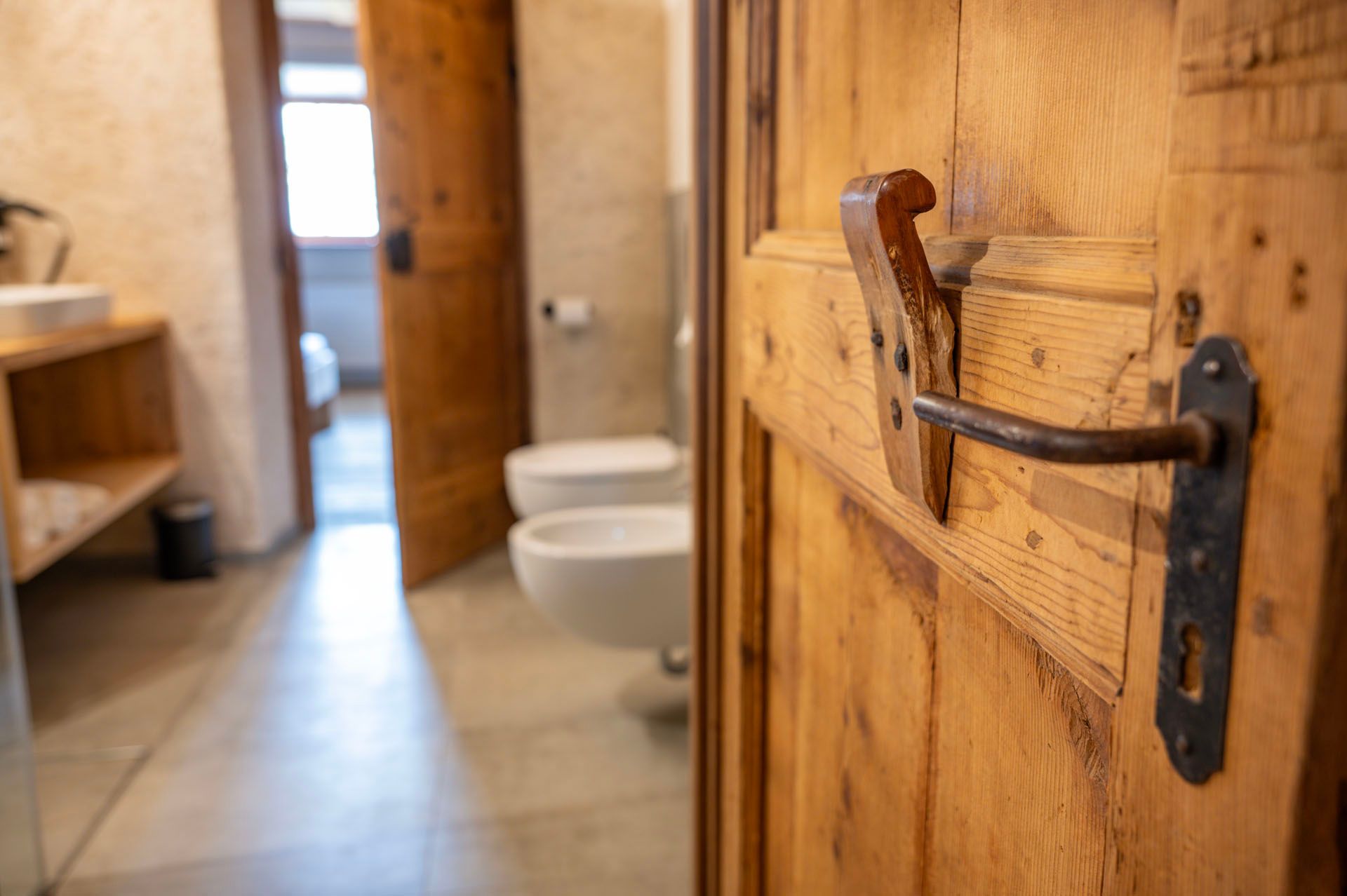Durch eine Holztür mit Metallgriff gelangt man in ein Badezimmer mit zwei Toiletten und einem Waschbecken.