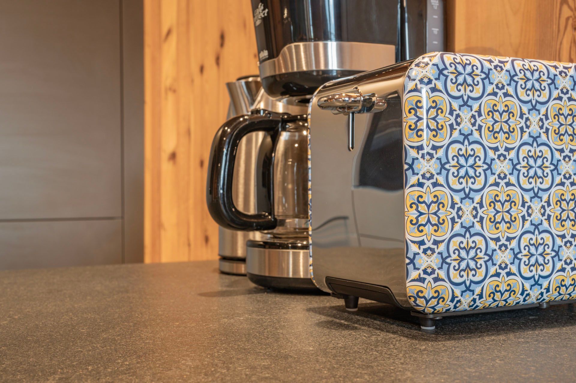 Ein Toaster mit einem blau-gelben Muster steht neben einer Kaffeemaschine auf einer Theke.
