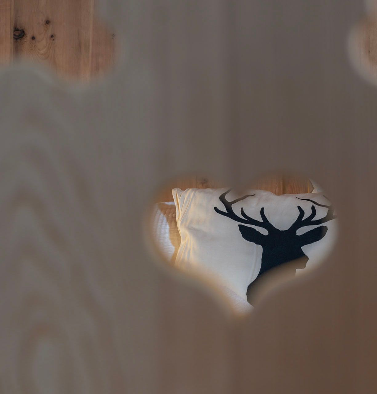 Hinter einem herzförmigen Loch in einem Holzzaun liegt ein Kissen mit einem Hirsch darauf.