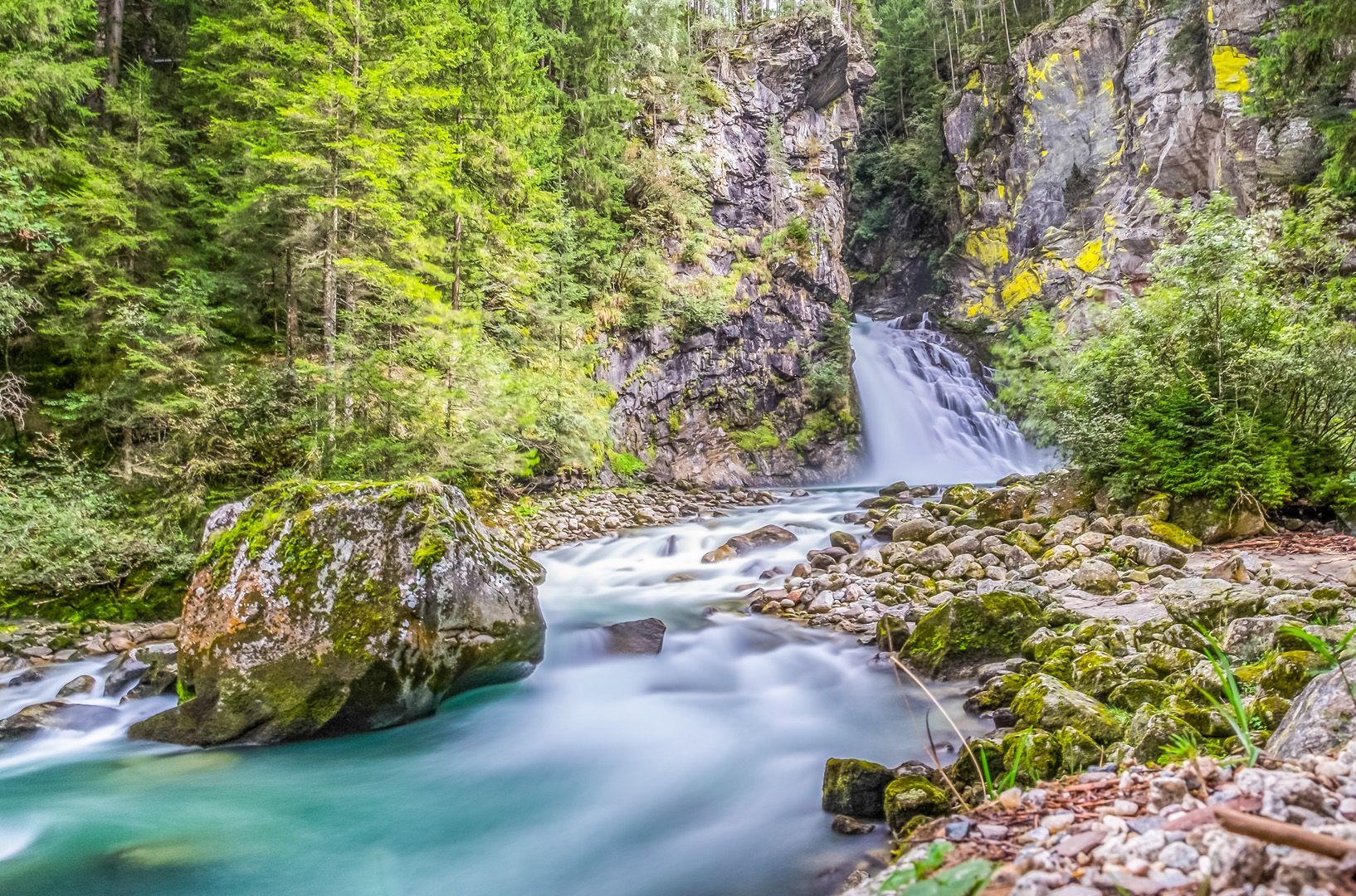 Ein Fluss, der durch einen üppigen grünen Wald fließt, mit einem Wasserfall im Hintergrund.