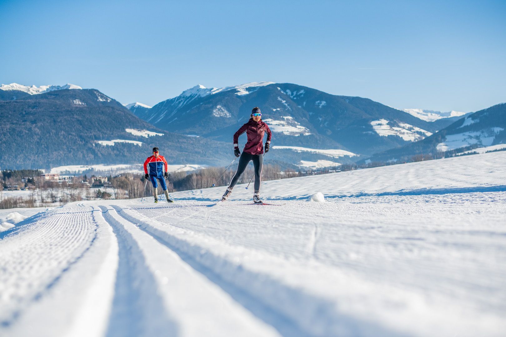 Zwei Personen laufen auf einer verschneiten Loipe in den Bergen Skilanglauf.