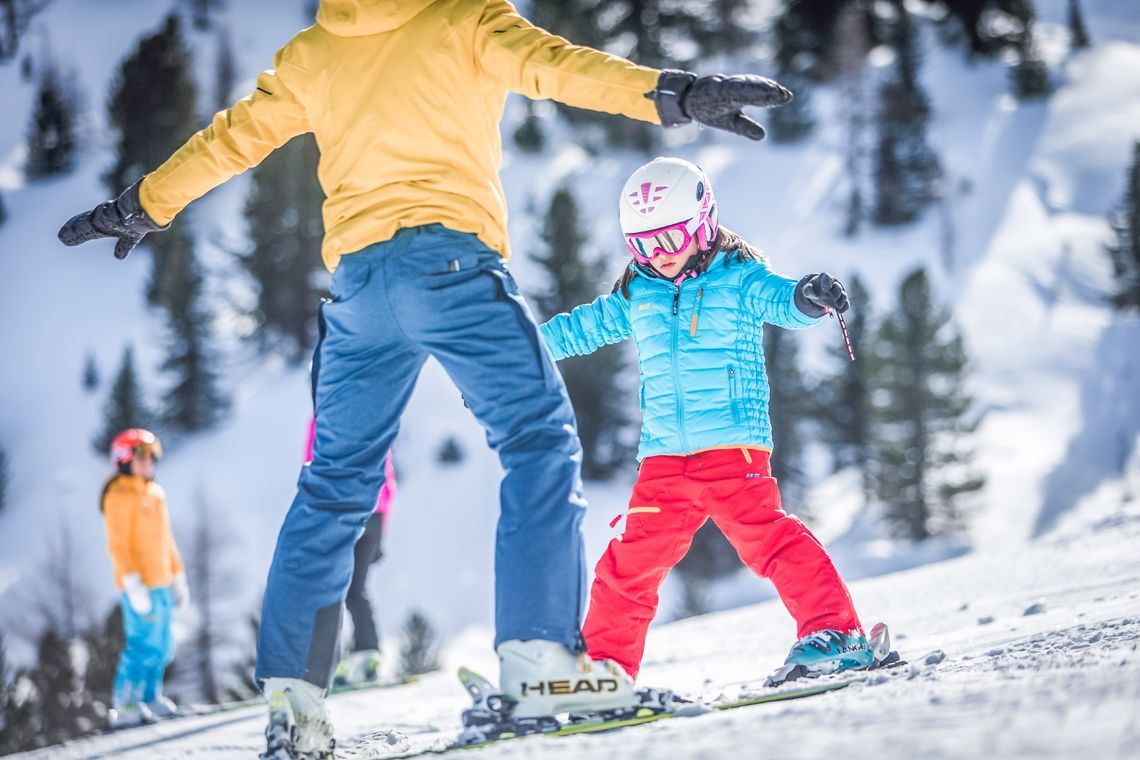 Ein Mann bringt einem kleinen Mädchen das Skifahren im Schnee bei.