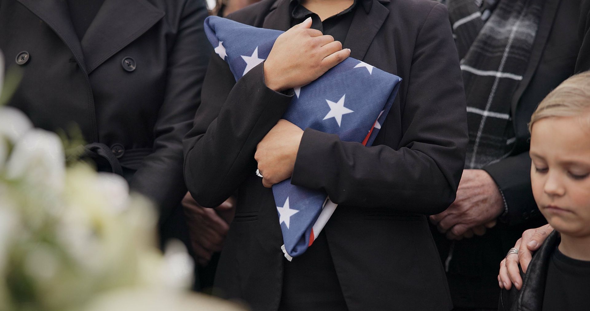 People holding a folded American flag at a somber outdoor ceremony