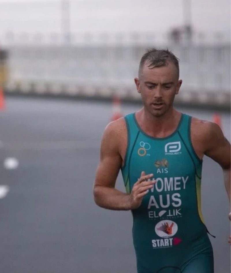 Close up shot of Liam competing in the run leg of a triathlon race. He is mid stride and wearing an Australian tri-suit wth his name and brand logos on the front.