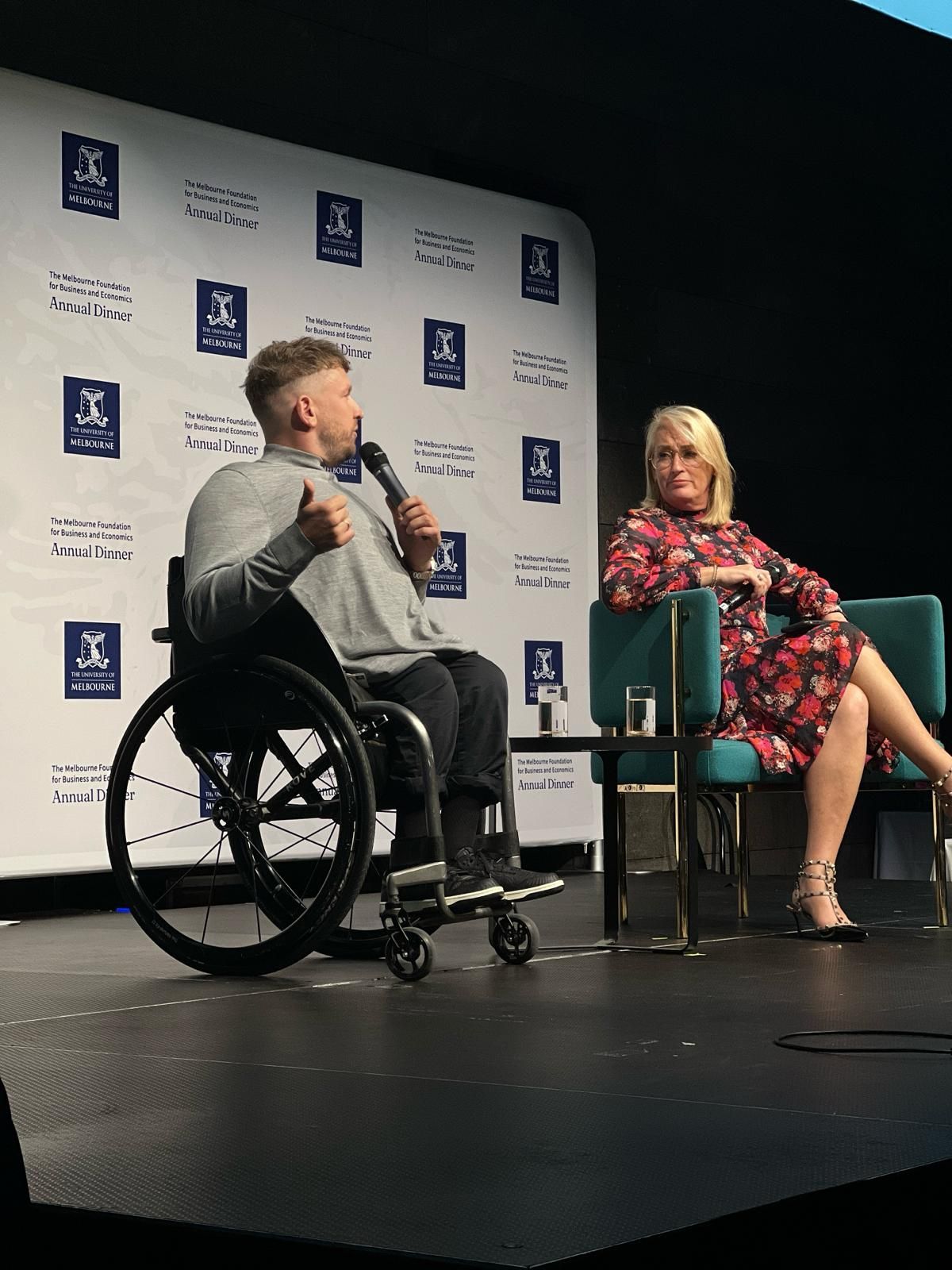 Dylan (left) with Sally Capp (right) on stage speaking into a microphone.