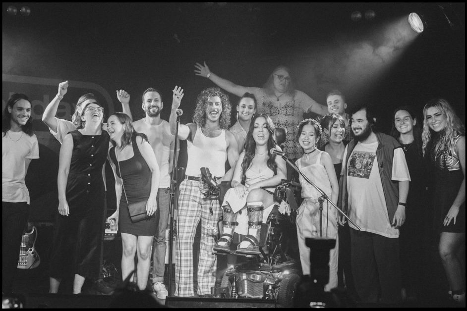 Black and white photo of recipient Dina (middle) surrounded on stage by a big crew of artists and staff.