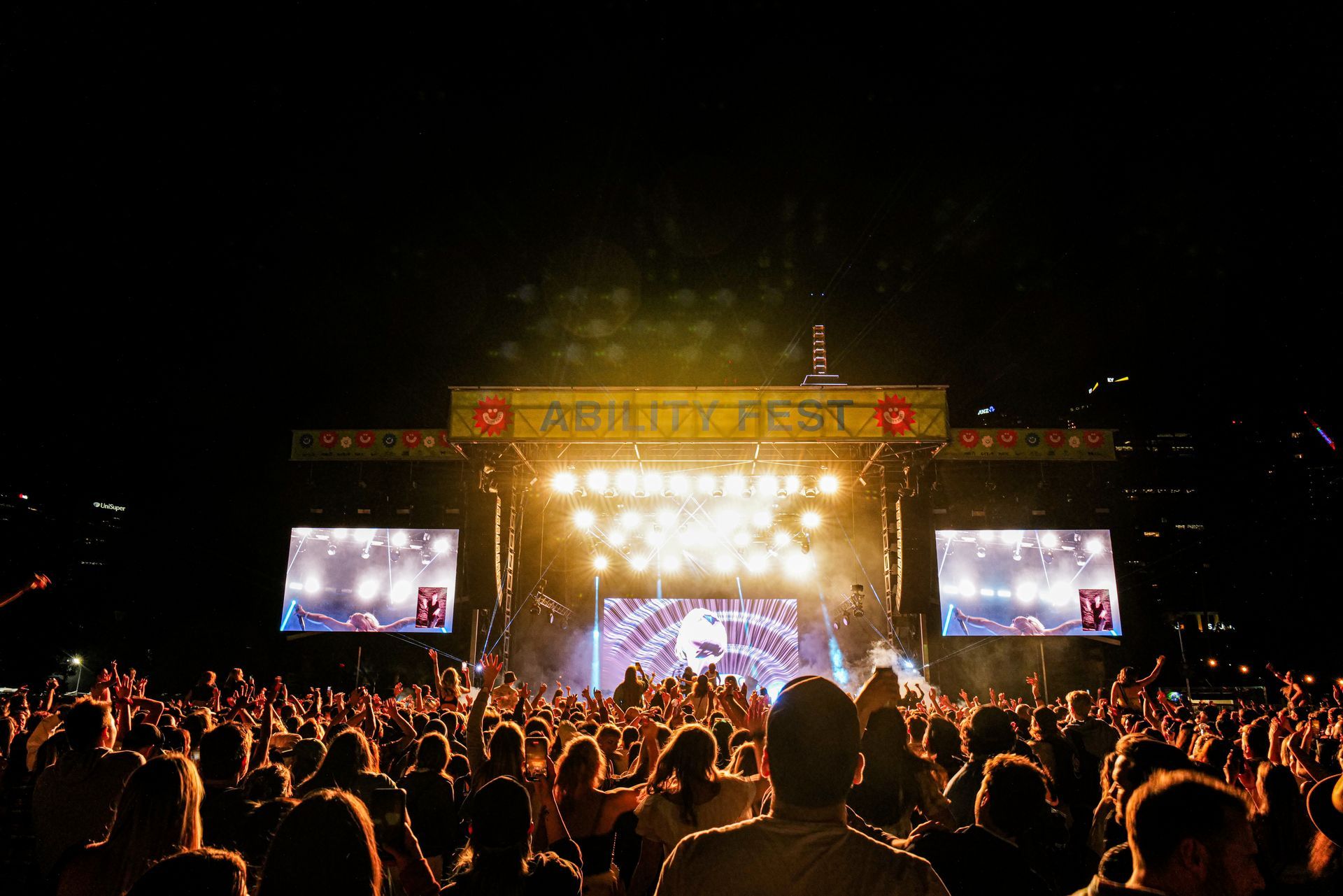 Night time shot of Ability Fest main stage and the back of the crowds heads. 
