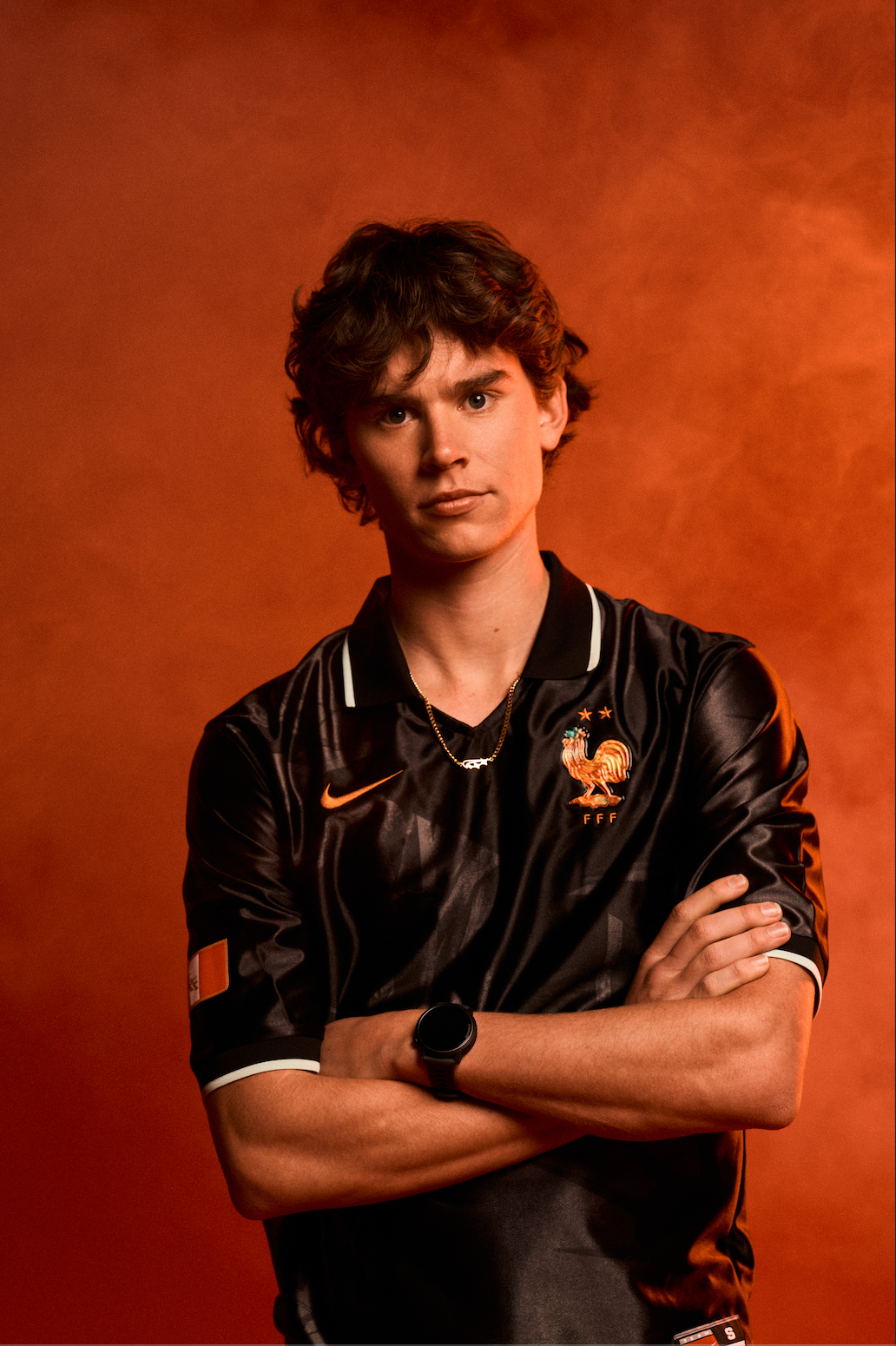 Studio image of Angus, crossing his arms, wearing Nike kit. He stands in front of a red background and smoke in the air.