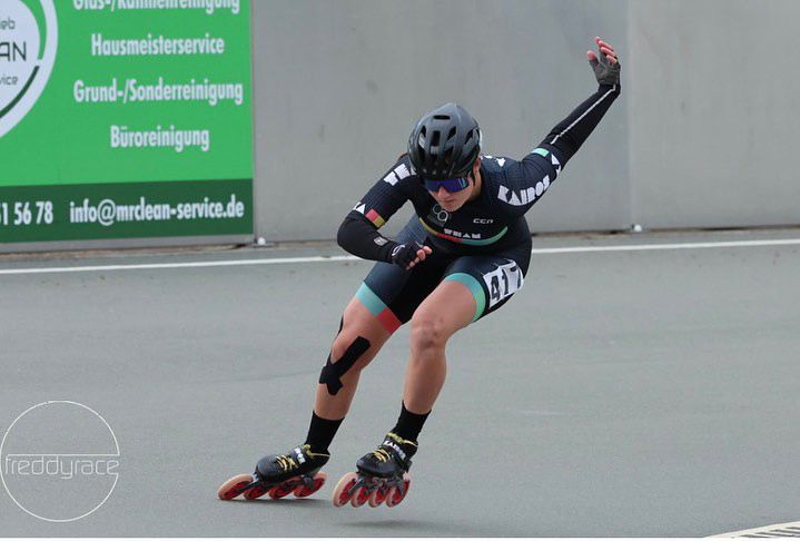 Recipient Asha mid race for inline speed skating. She wears a helmet, lycra, skates and gloves. One arm is raised behind her in the air.