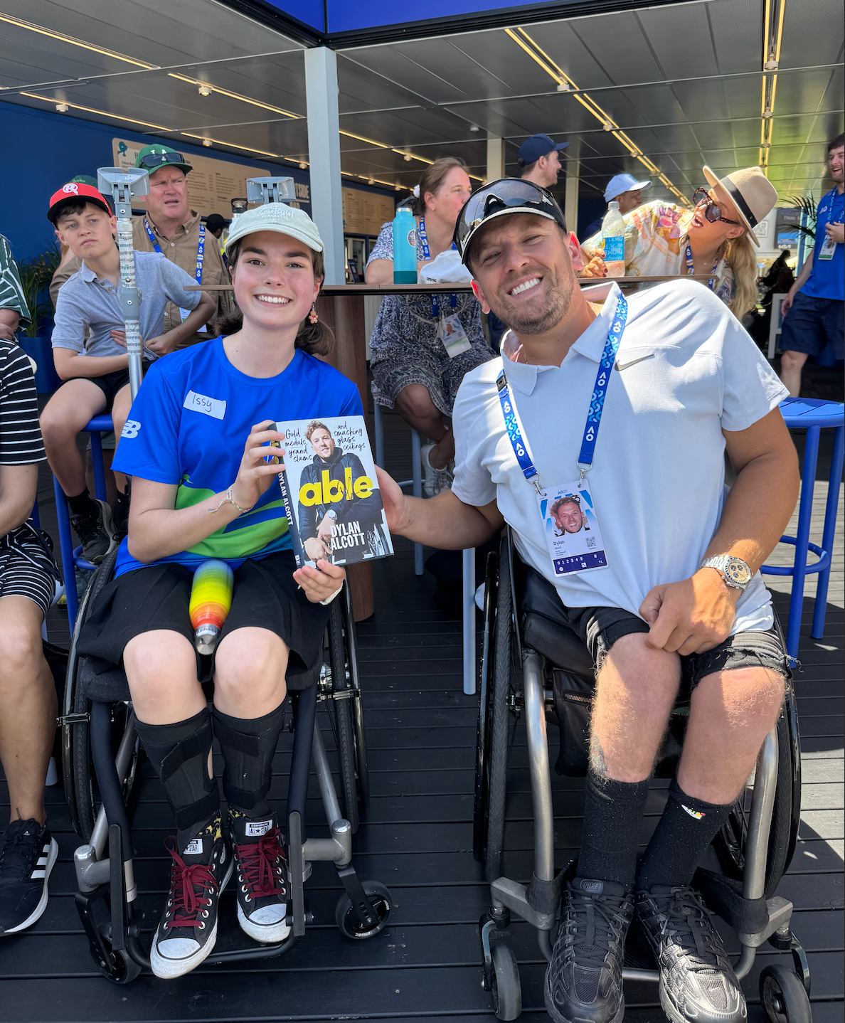 A young female (left) and Dylan (right) smile to the camera holding the ListenABLE book between them. They both are wheelchair users.