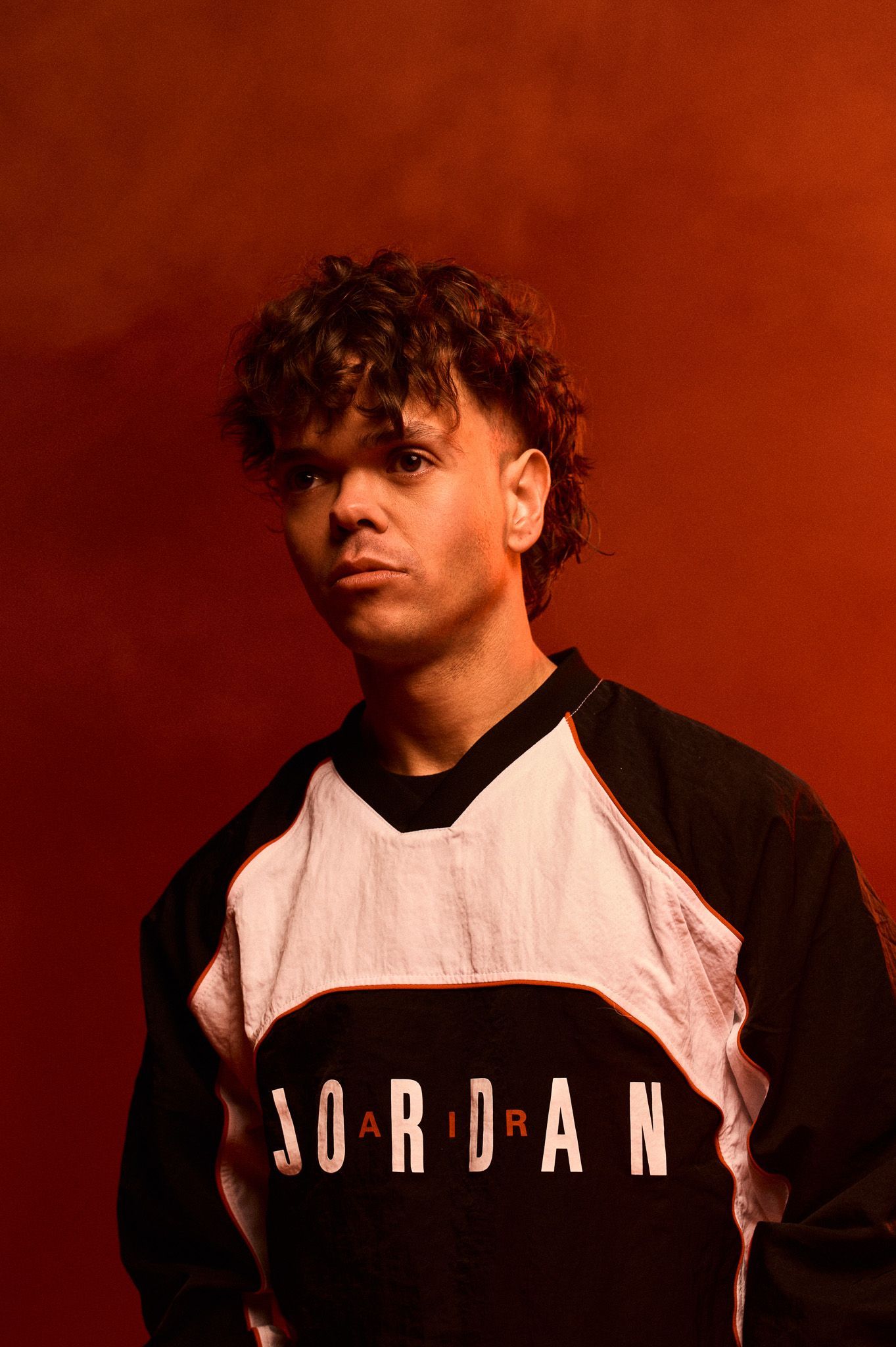 Studio image of Daniel, arms by his side, wearing Nike kit. He stands in front of a red background and smoke in the air.