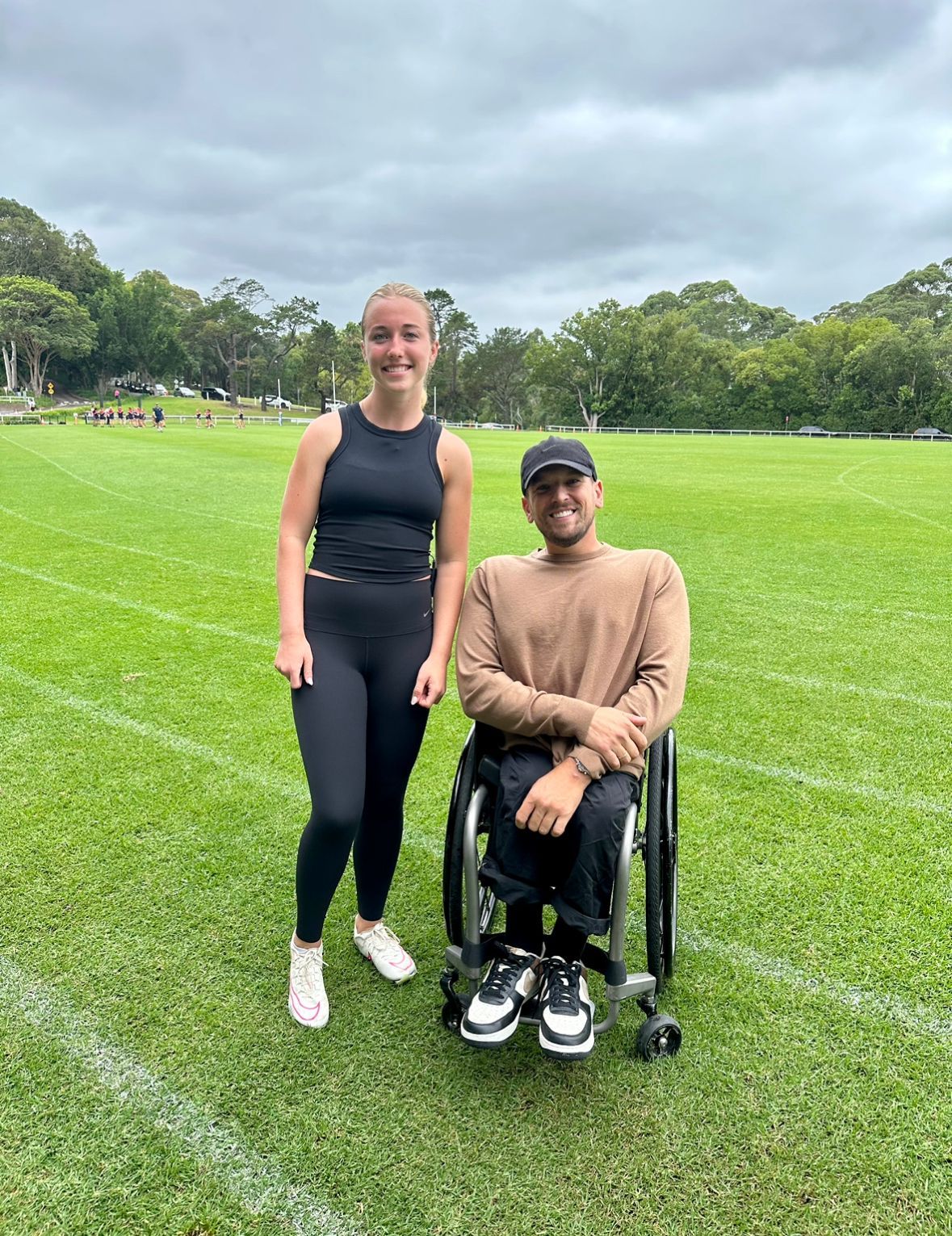 Sybella (left) and Dylan (right) smile to camera side by side. The photo is taken outside on a grass oval with a white painted athletics track around the perimeter.
