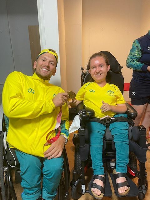 Dylan (left) and recipient Jamieson (right) wear yellow Aussie uniforms holding Paralympic gold medal. Both are wheelchair users. 