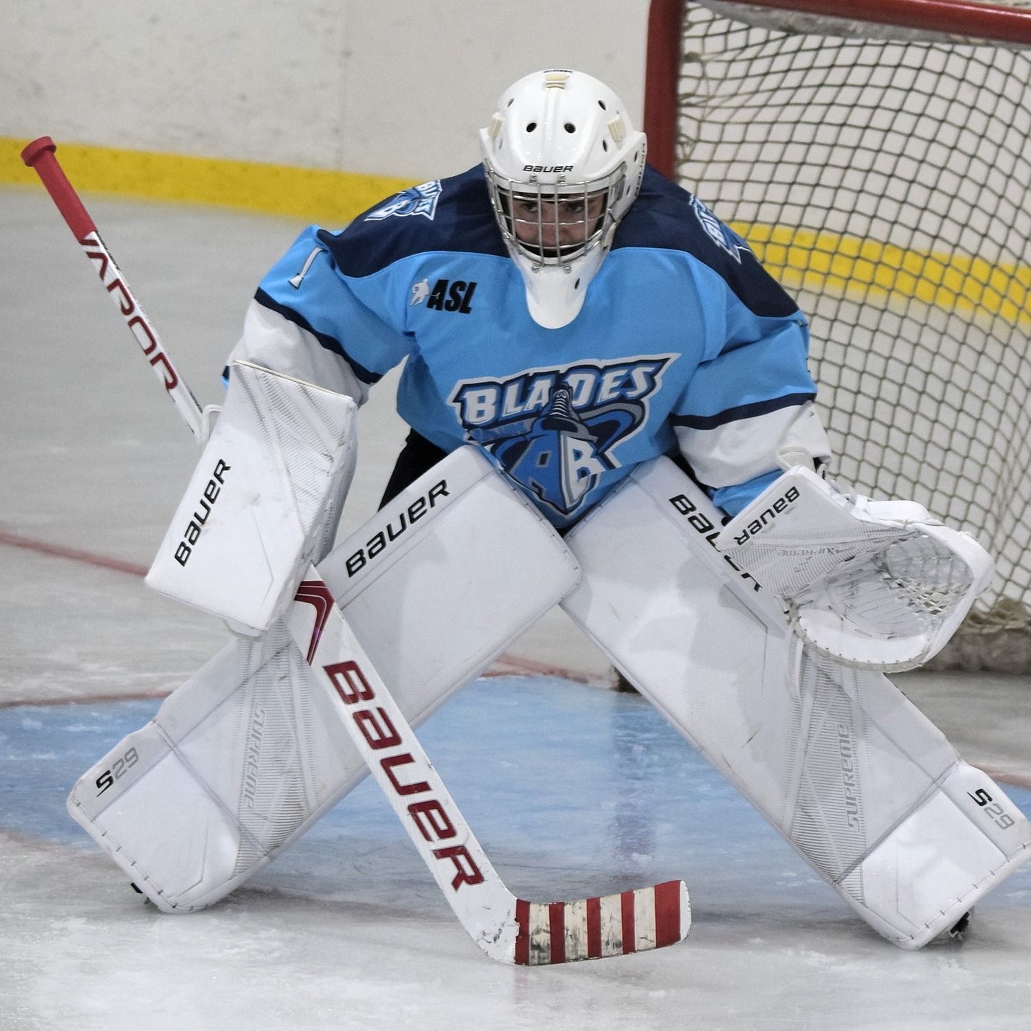 Lachlan pictured in front of an ice hockey next, wearing ice hockey goalie pads, gloves, helmet, jersey and holds hockey stick.