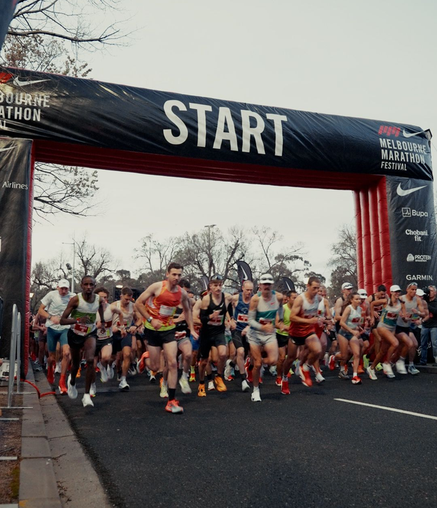 Blurred photo of a large group of runners starting at the finish line for the Melbourne marathon. Many are mid stride.