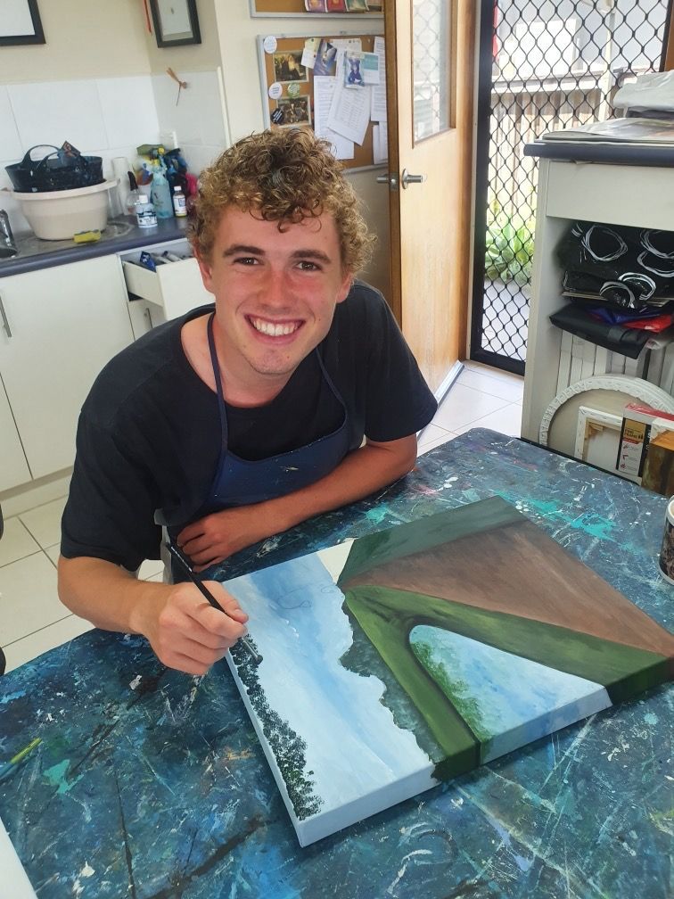 Recipient Sam smiling to camera whilst working on his painting.