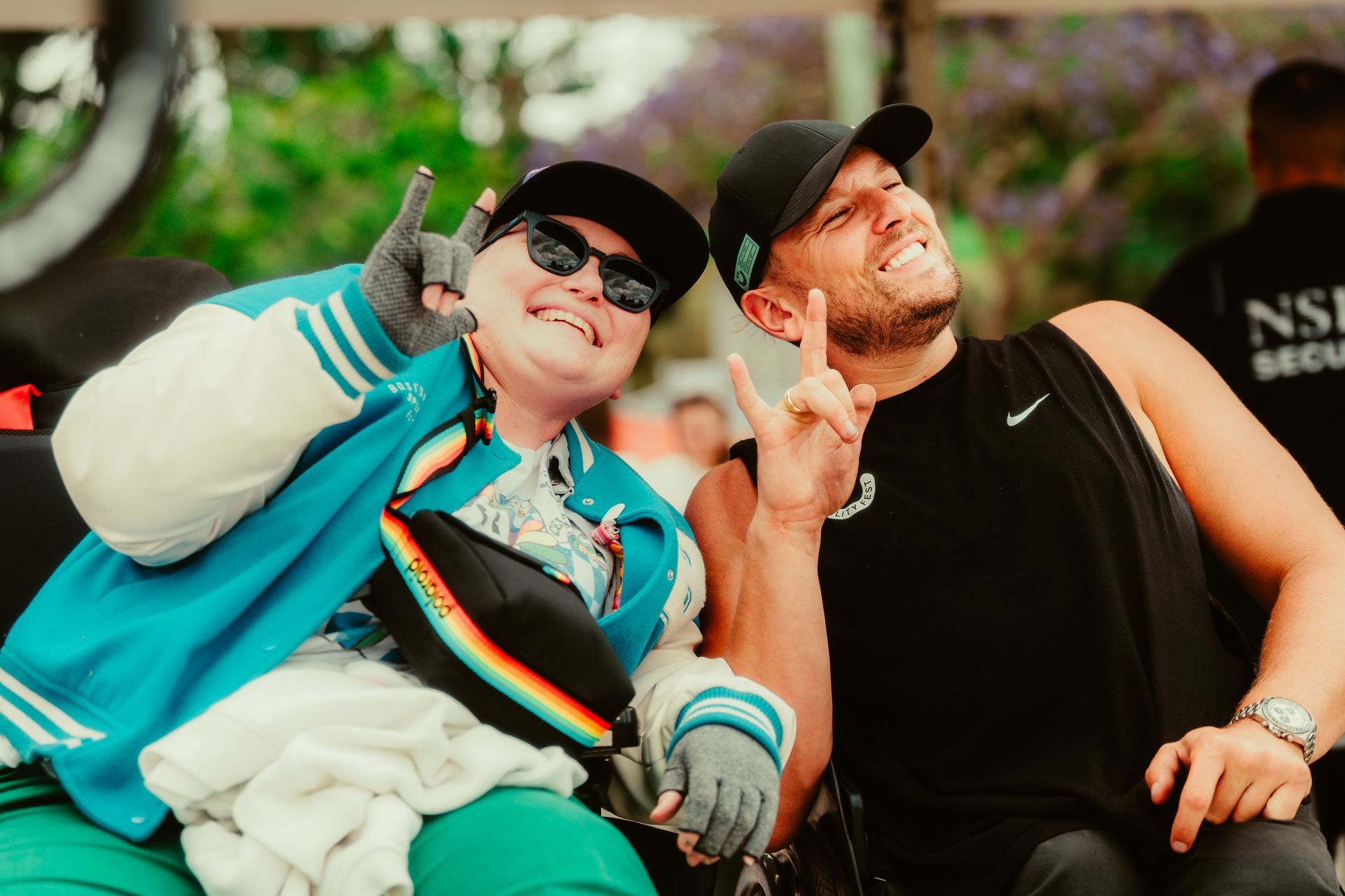 Dylan and a woman who are both wheelchair users pose for a photo with the rock sign in one hand.