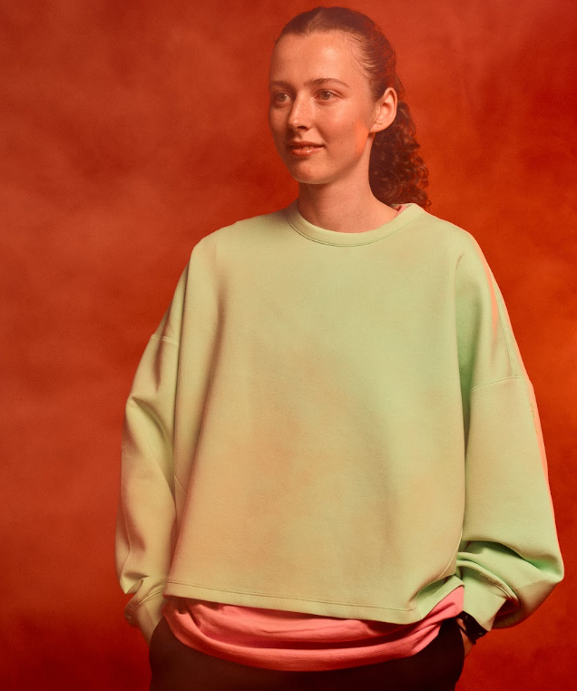 Studio image of Annabelle, with arms in her pockets, wearing Nike kit. She stands in front of a red background and smoke in the air.