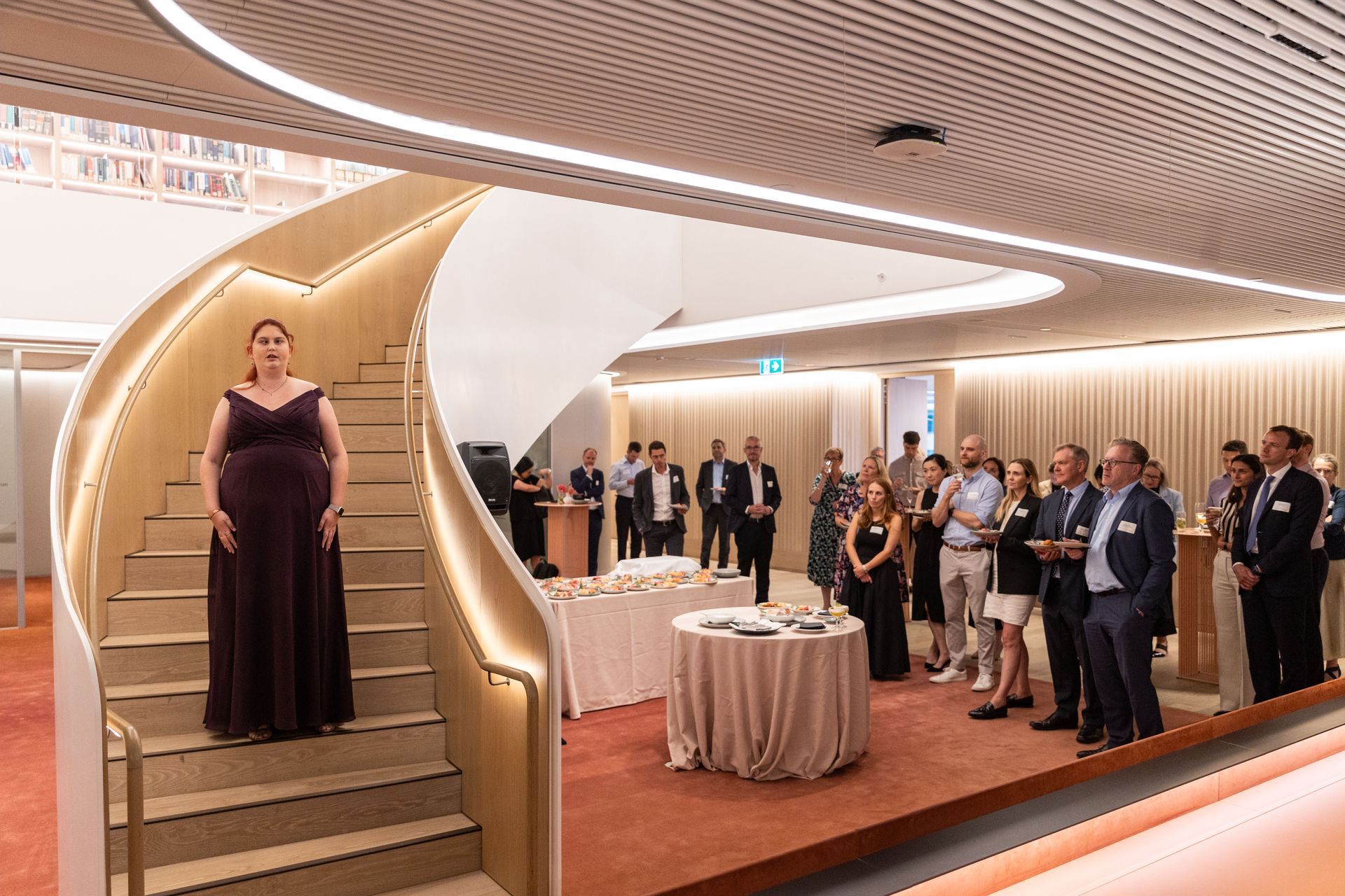 Recipient Kirsten singing on a large spiral staircase whilst the crowd watches in the background.