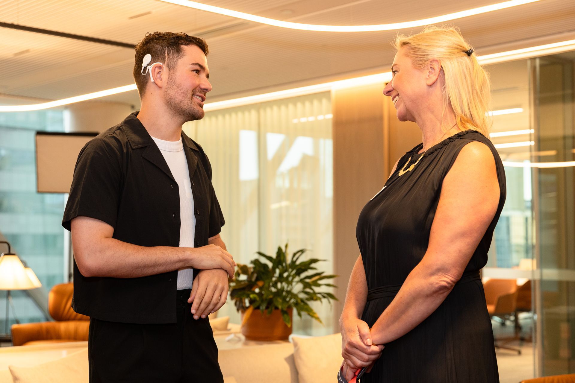 Side shot of DAF ambassador Nathan talking to Ashurst member. Nathan wears a white cochlear implant.