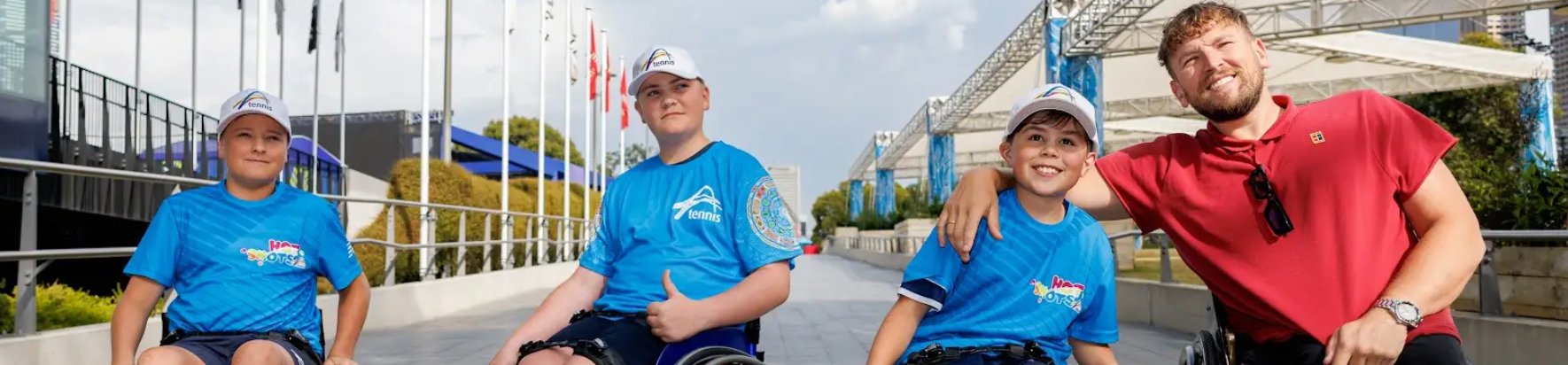 Three junior tennis boys at the Aus Open wear blue shirts and are in wheelchairs. Dylan (far right) loops his arm around the closest.