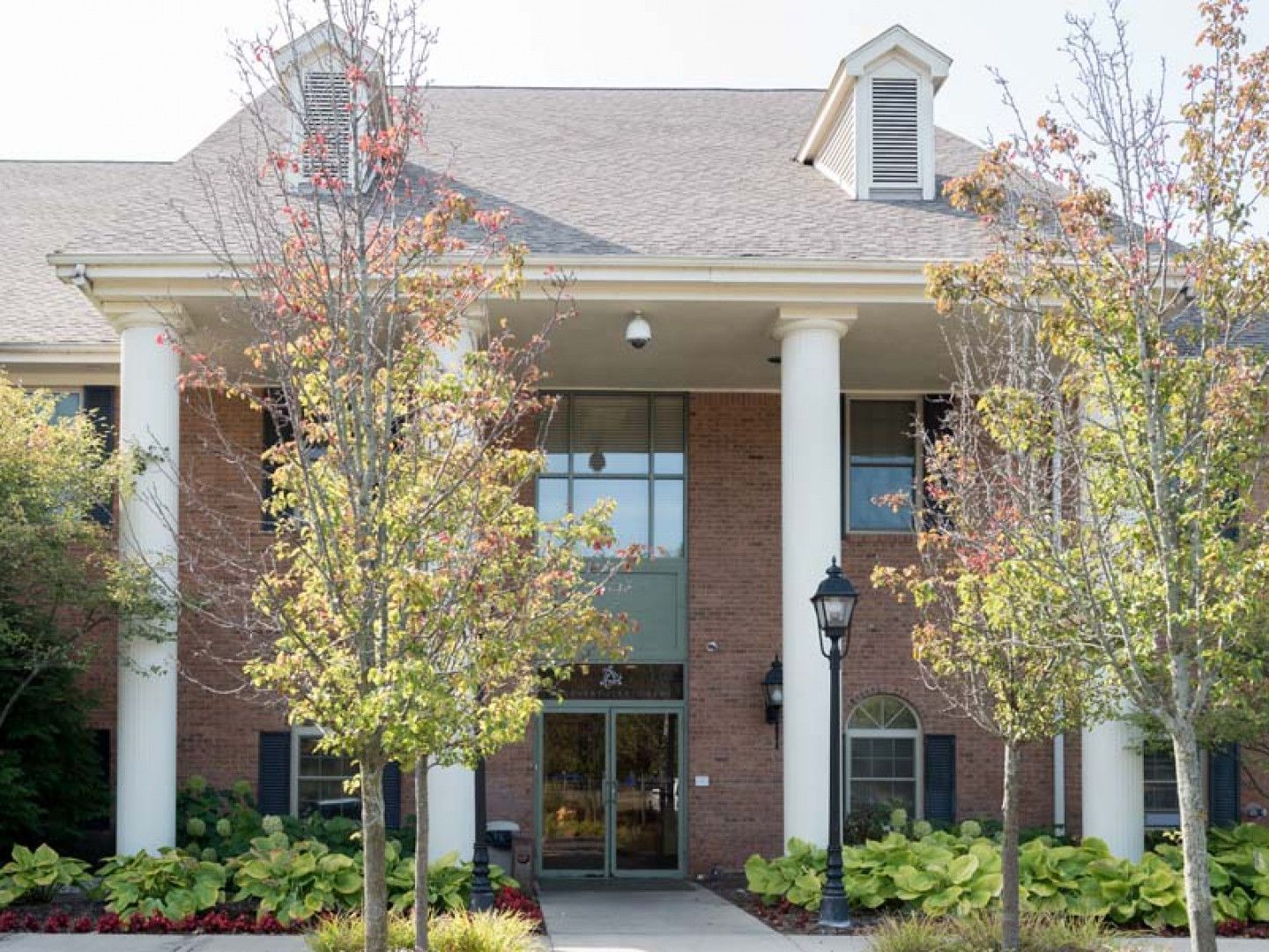 Brick building with large columns, glass doors, and trees in front.