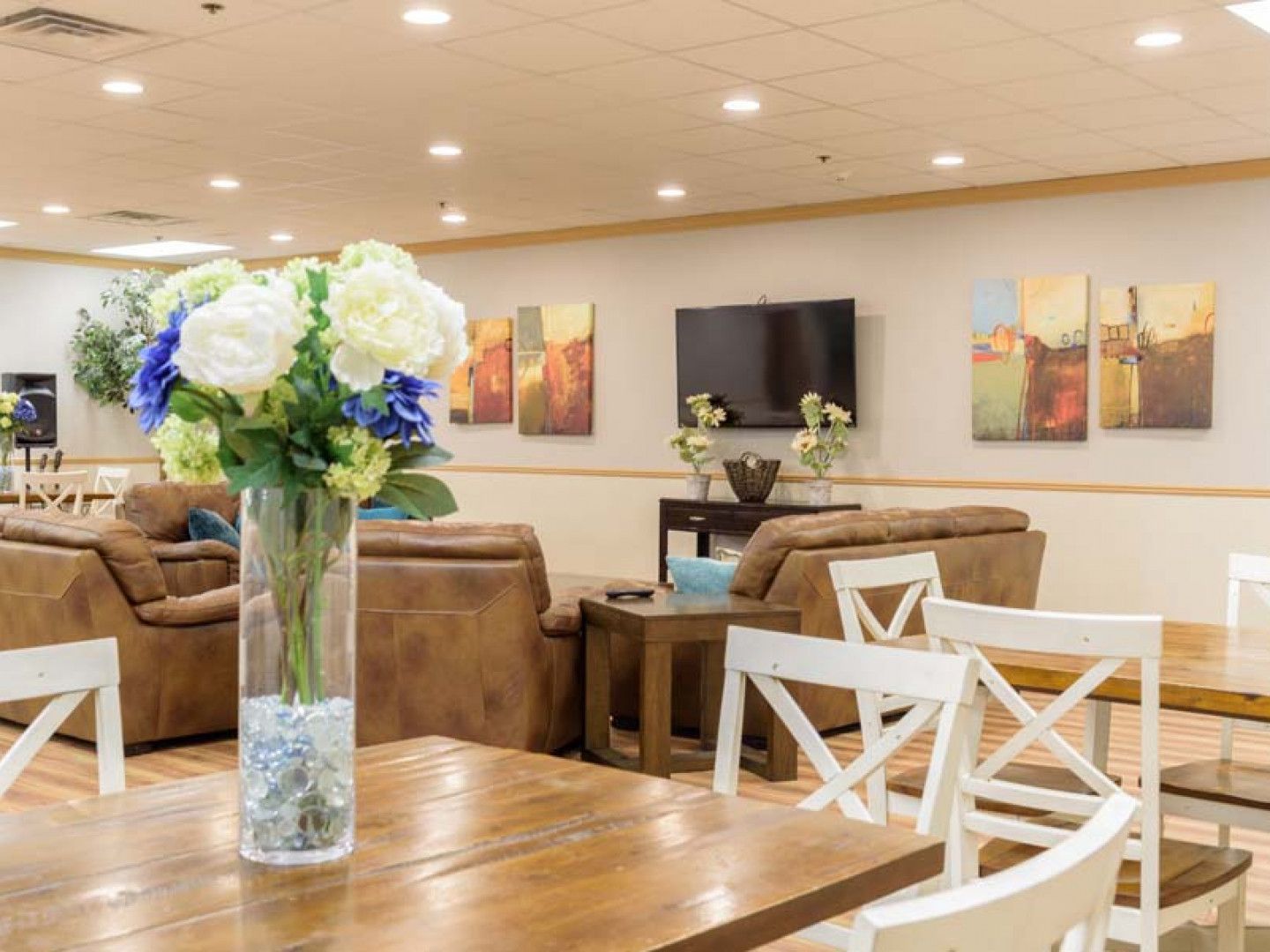Bright living room with tan sofas, white chairs, wooden table, and vase of white and blue flowers.