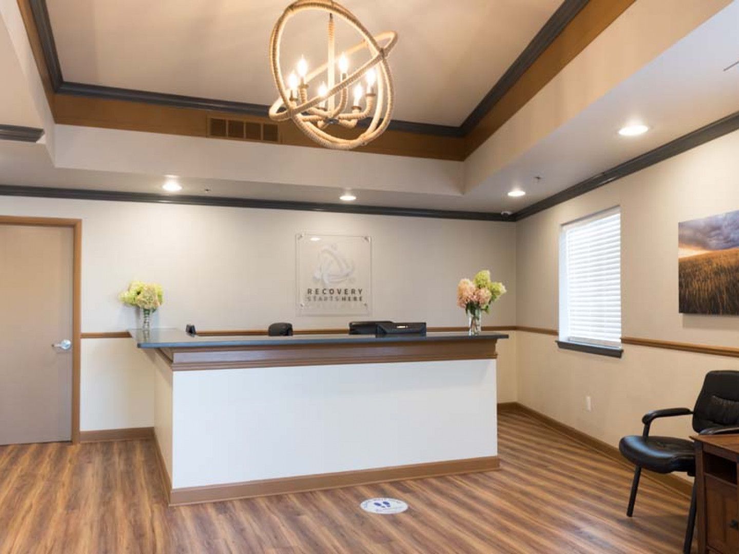 Reception area with a desk, floral arrangements, and a modern chandelier.