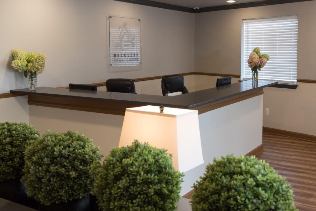 Empty reception desk with black chairs, beige walls, and potted greenery in a modern office lobby