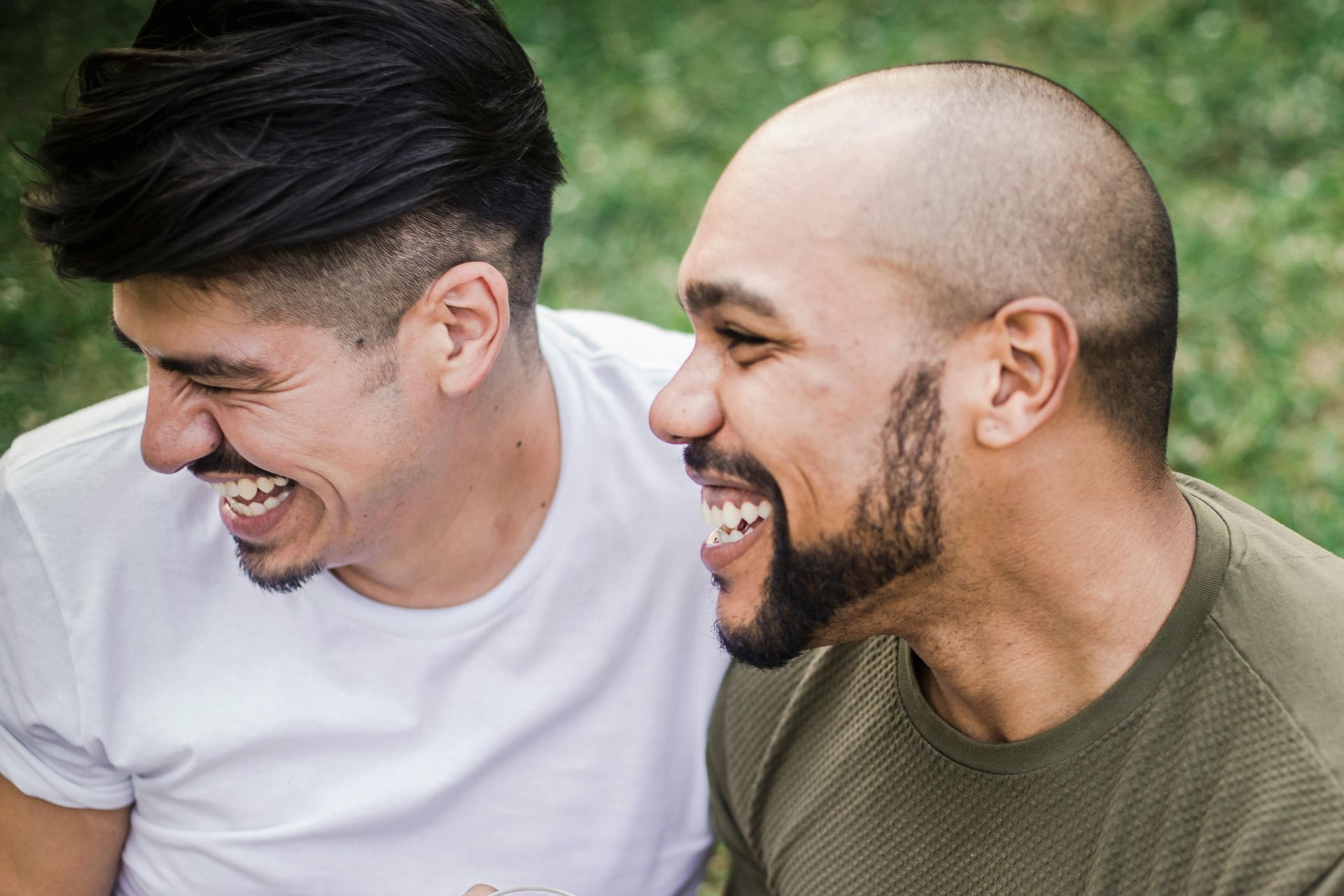 Two men smiling and laughing outdoors, one with dark hair, one with a beard and buzz cut.