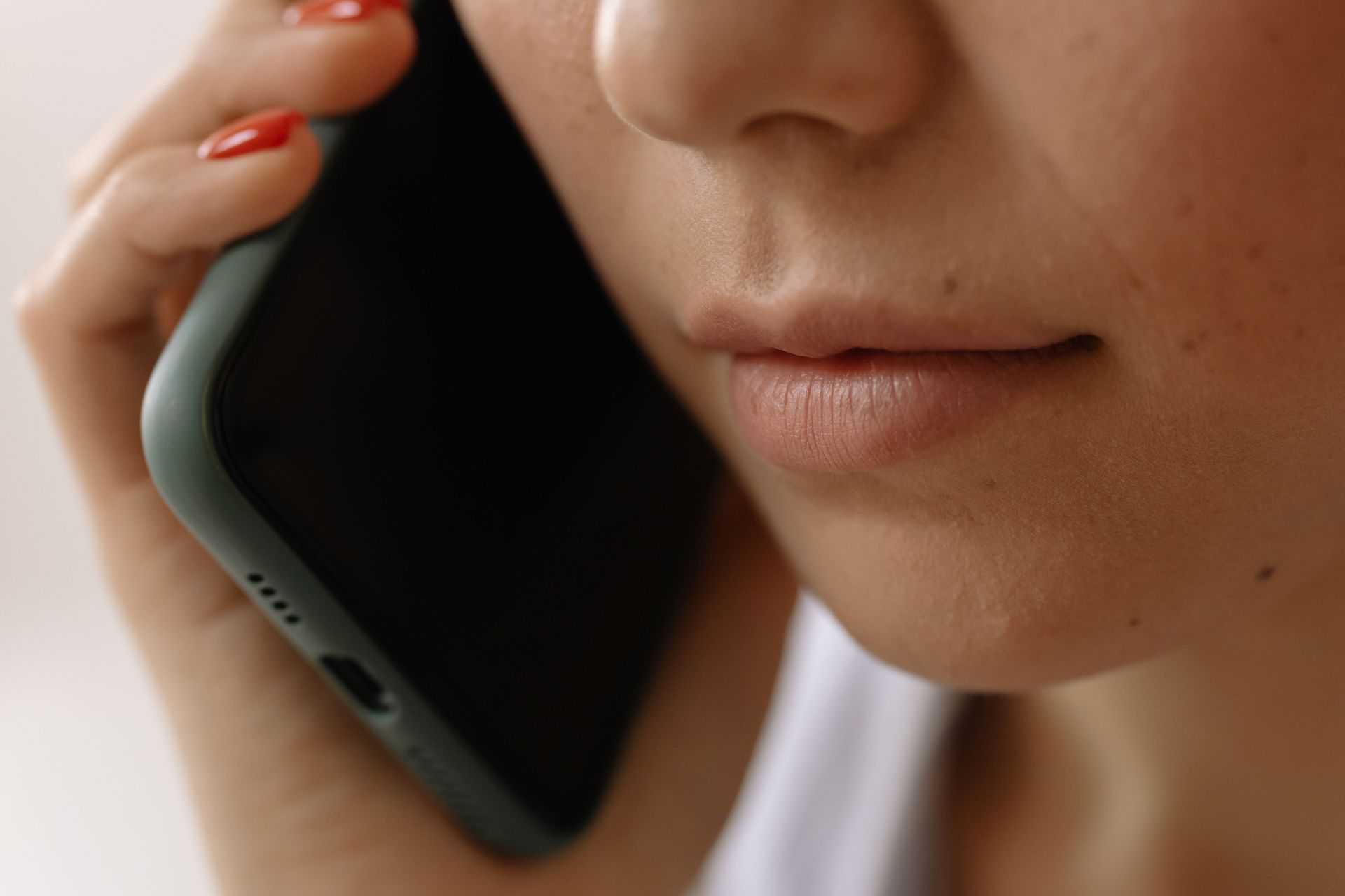 Person holding a smartphone to their ear, close-up of lower face with red nail polish