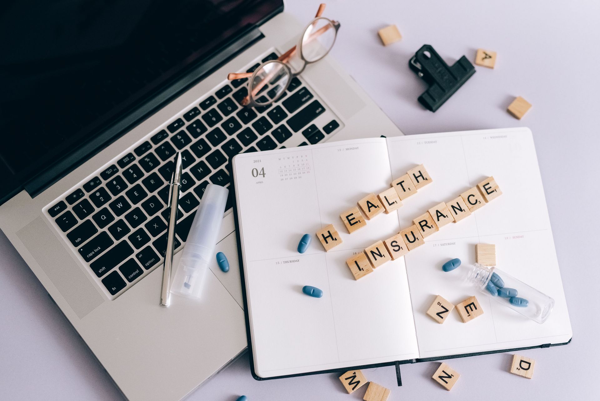 Open notebook with “health insurance” tiles on a laptop desk with glasses, pen, and small objects