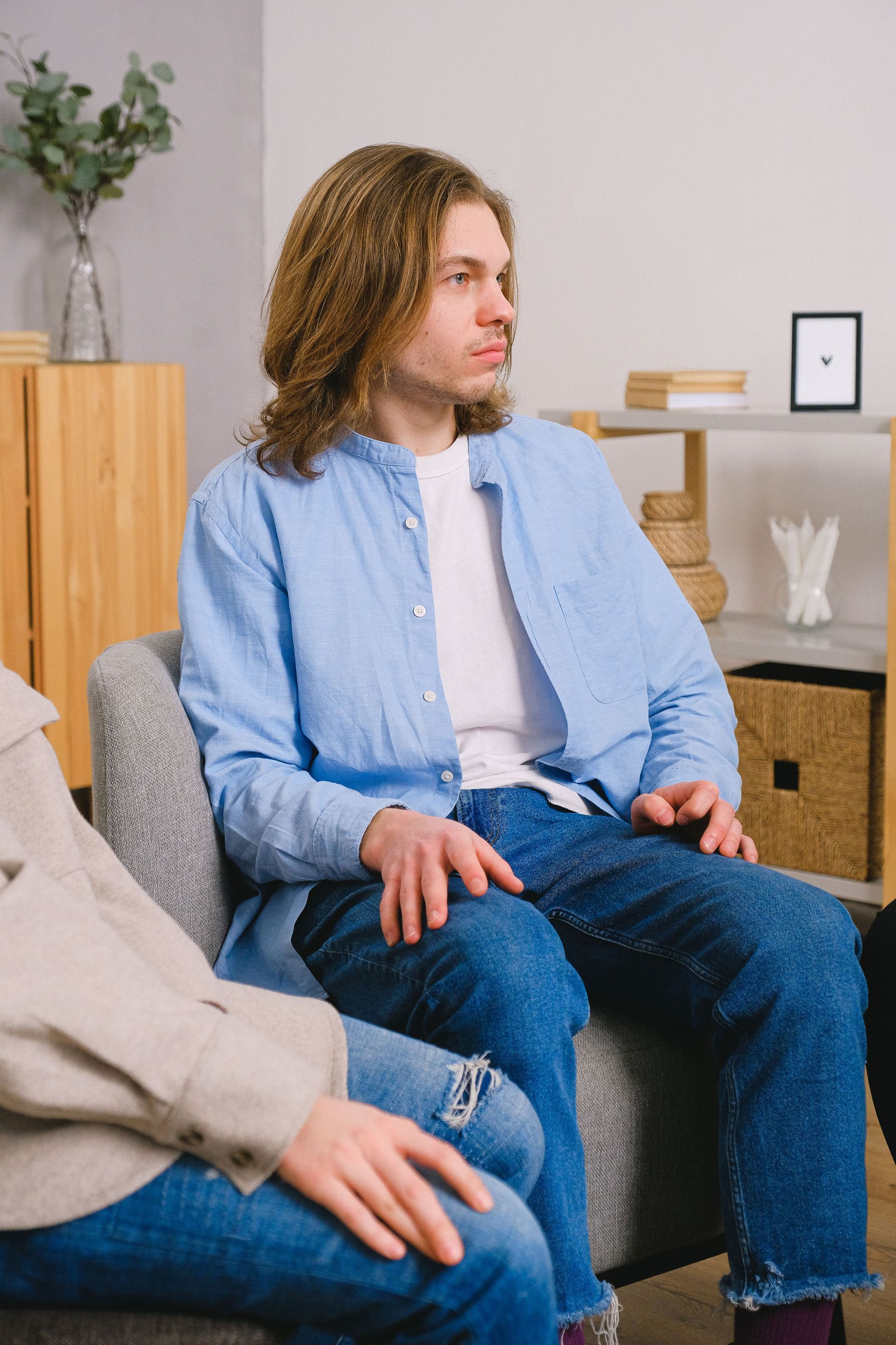 Two people seated in a living room, one in a blue shirt and jeans, facing left.