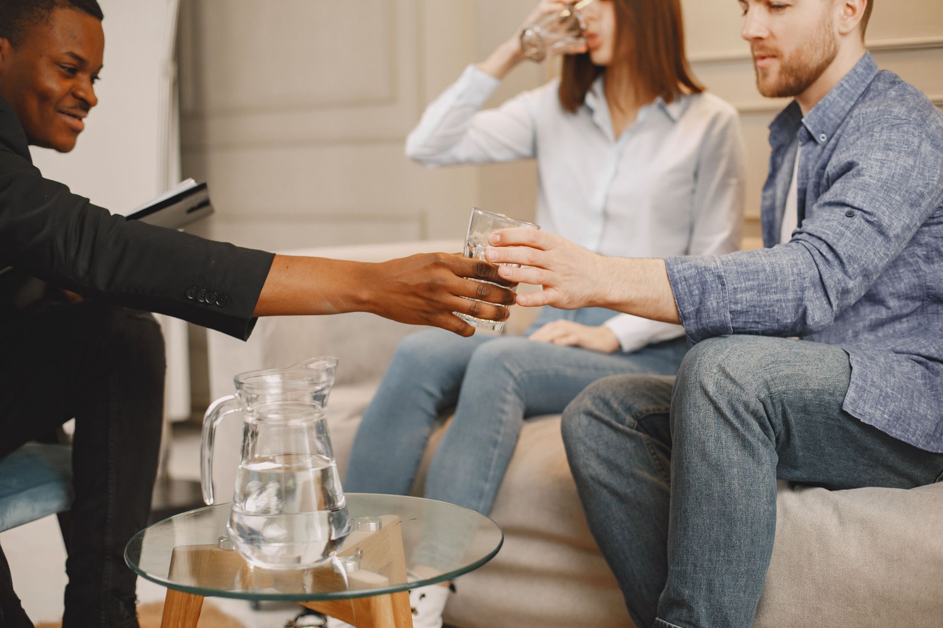 Three people sitting on a couch share drinks in a living room setting