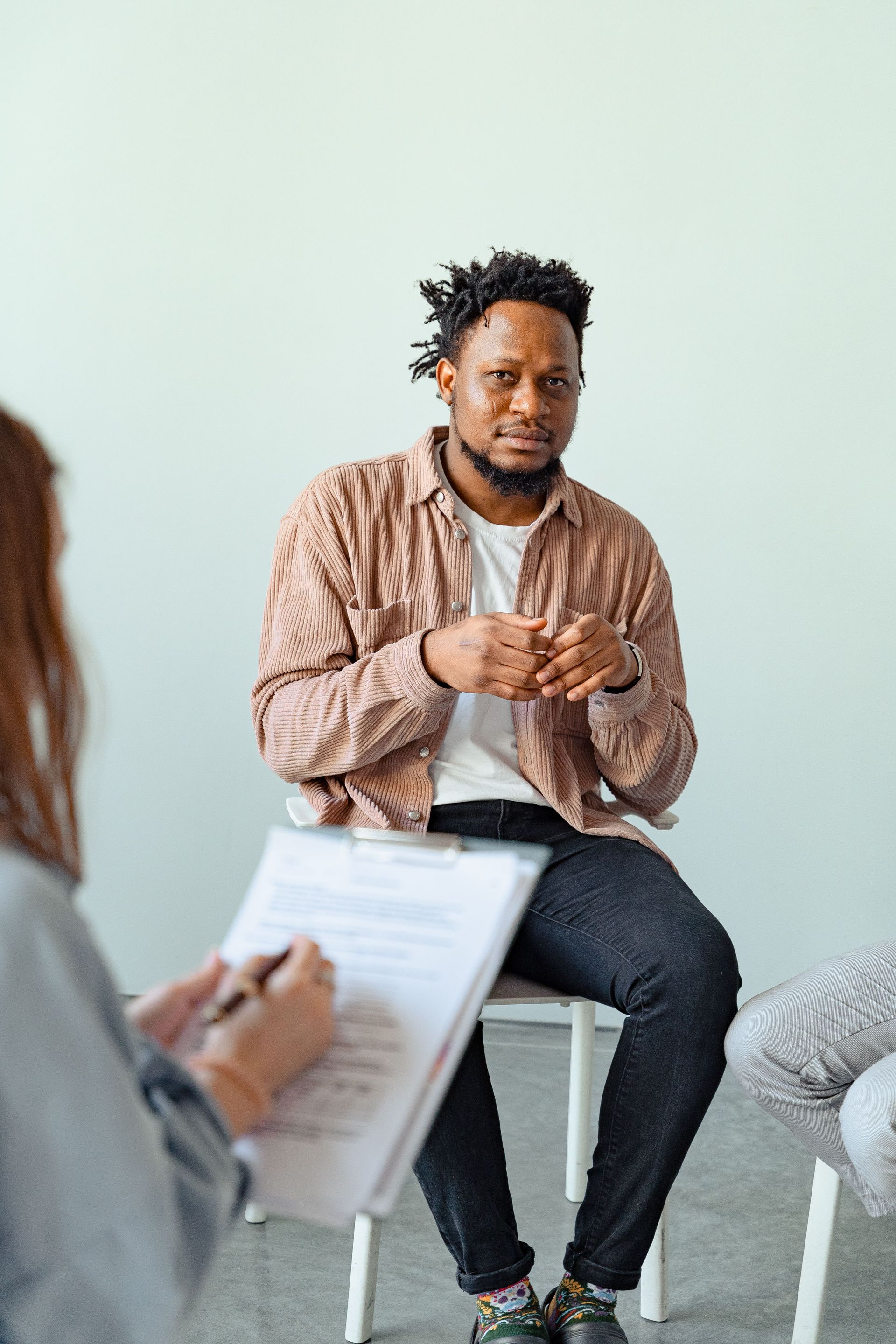 Man speaking in a small group discussion, seated with hands clasped, while others listen and take notes.
