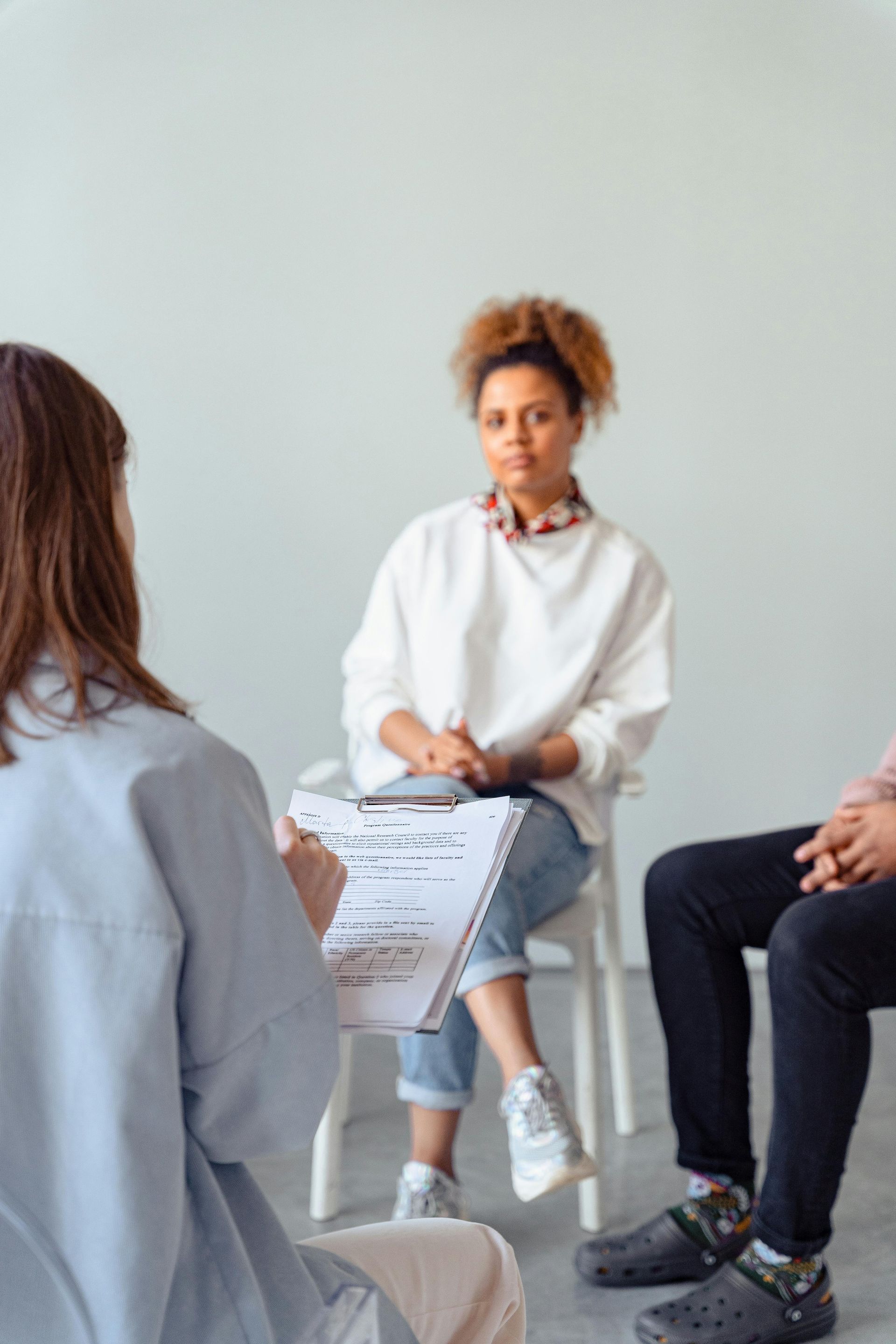 Small group in a discussion circle, with a woman holding notes in a bright room.