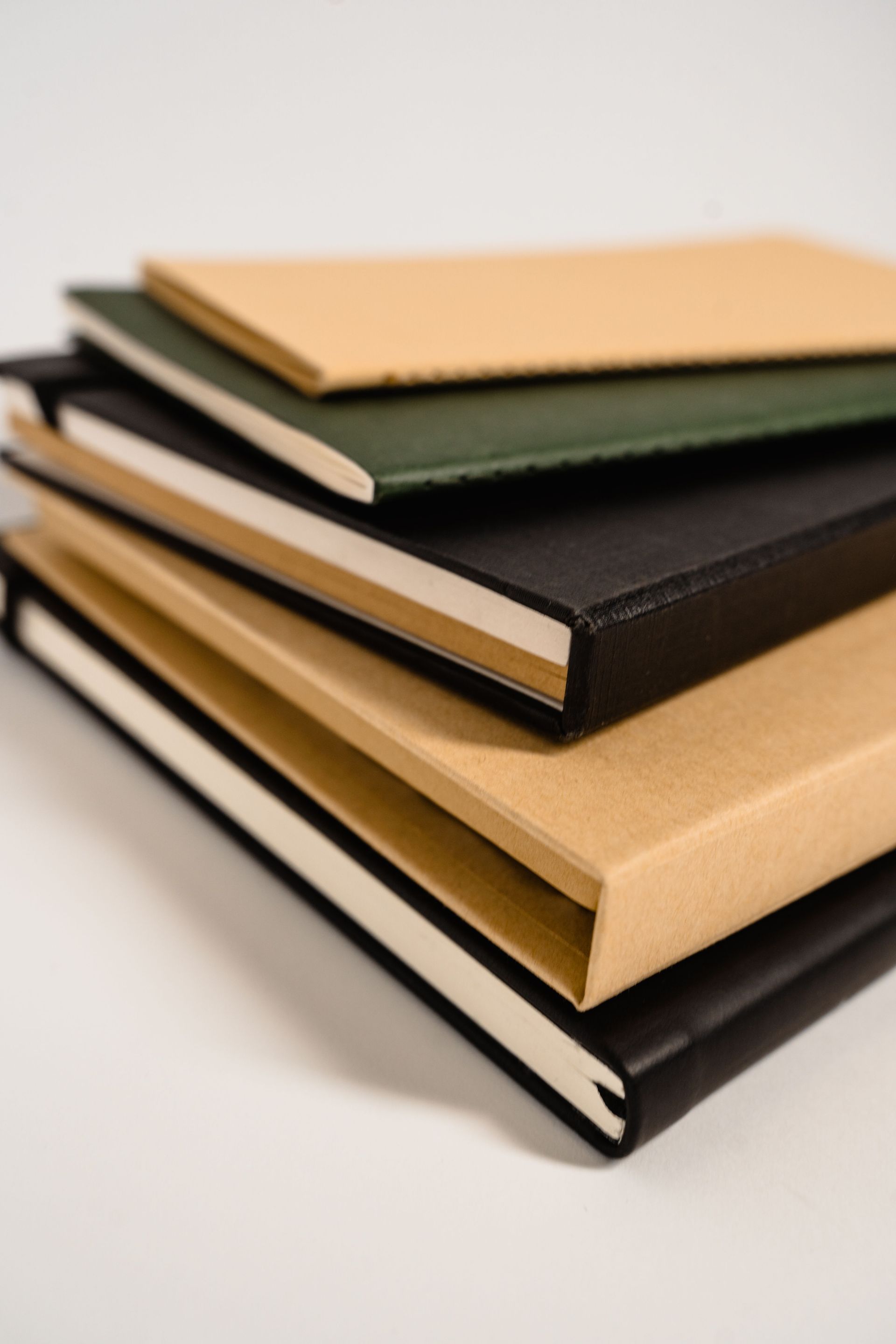 Stack of four notebooks with tan, green, and black covers on a white background