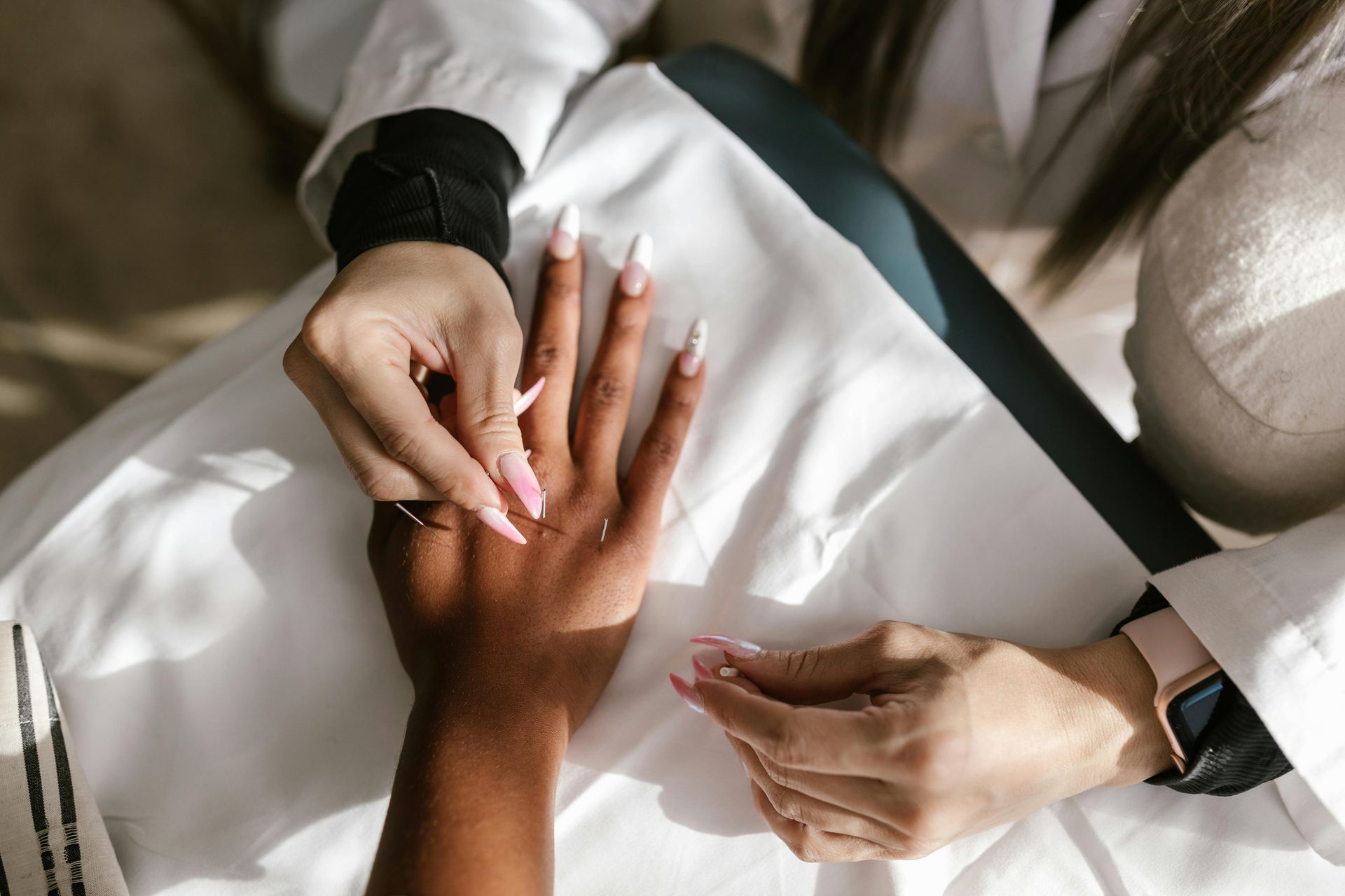 Hands receiving a manicure on a white towel, with pink nails being shaped by a nail file.
