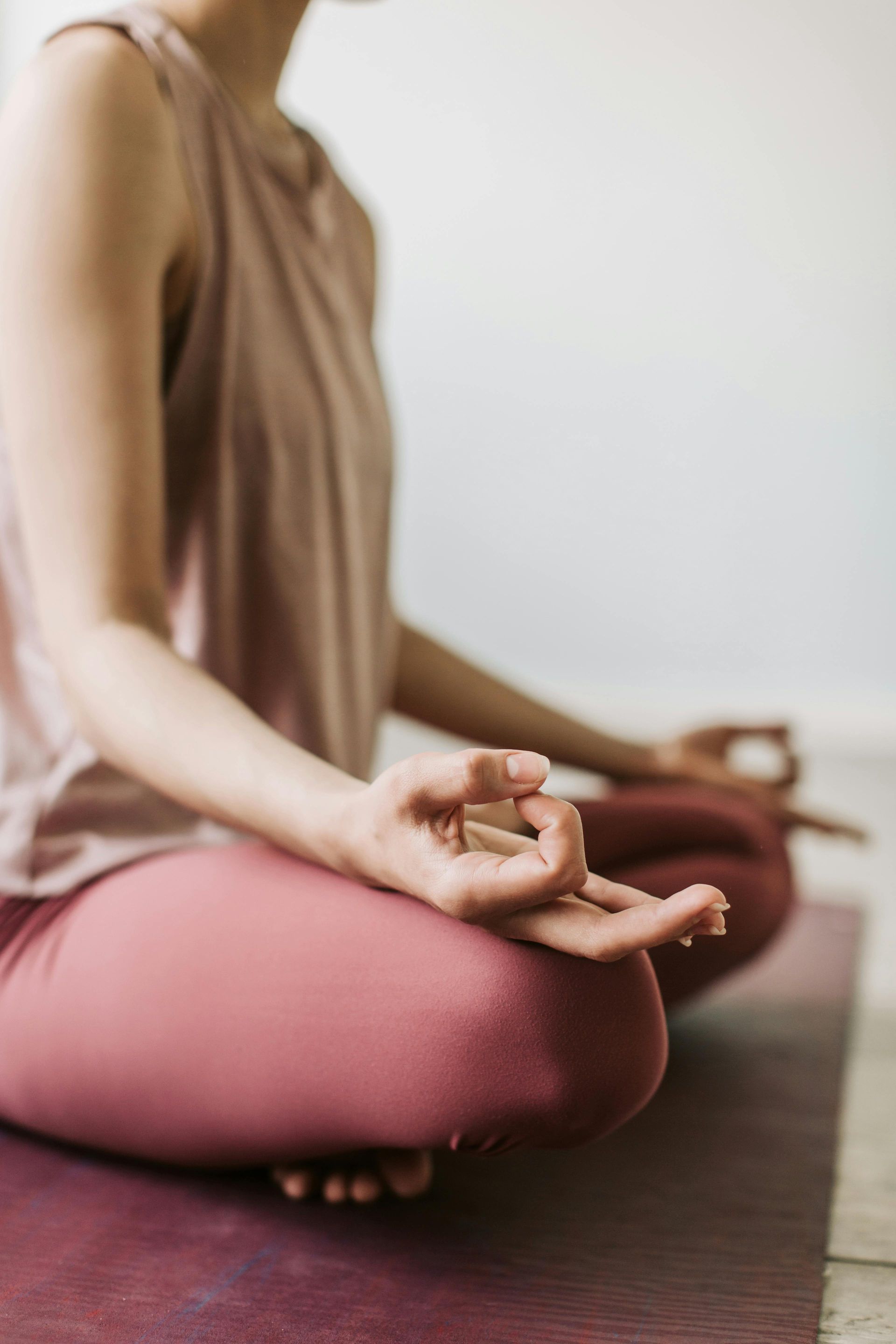 Person meditating cross-legged on a yoga mat indoors, hands resting in a mudra pose.