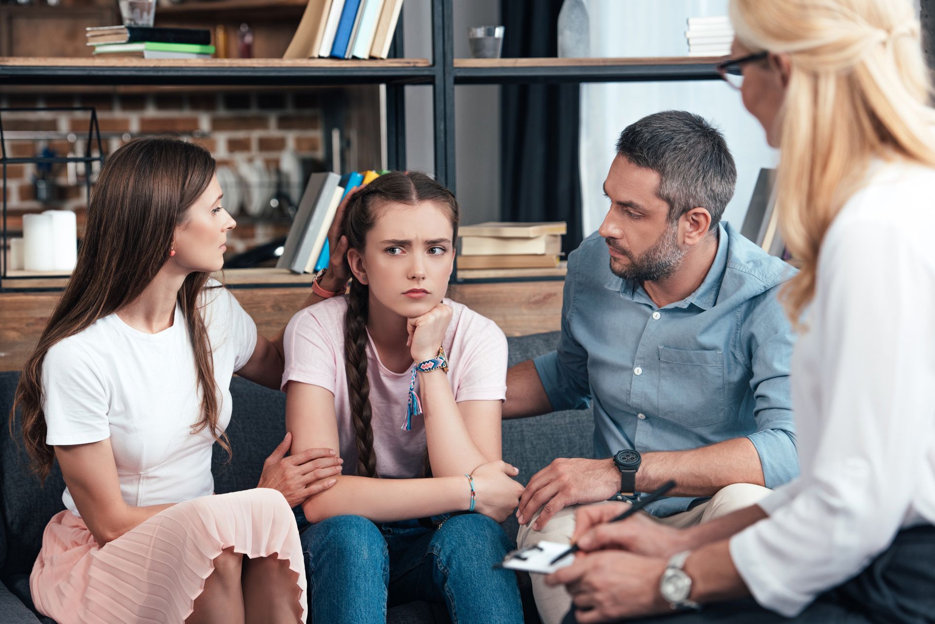 Three people in a counseling session, seated closely and talking with a therapist in a living room.