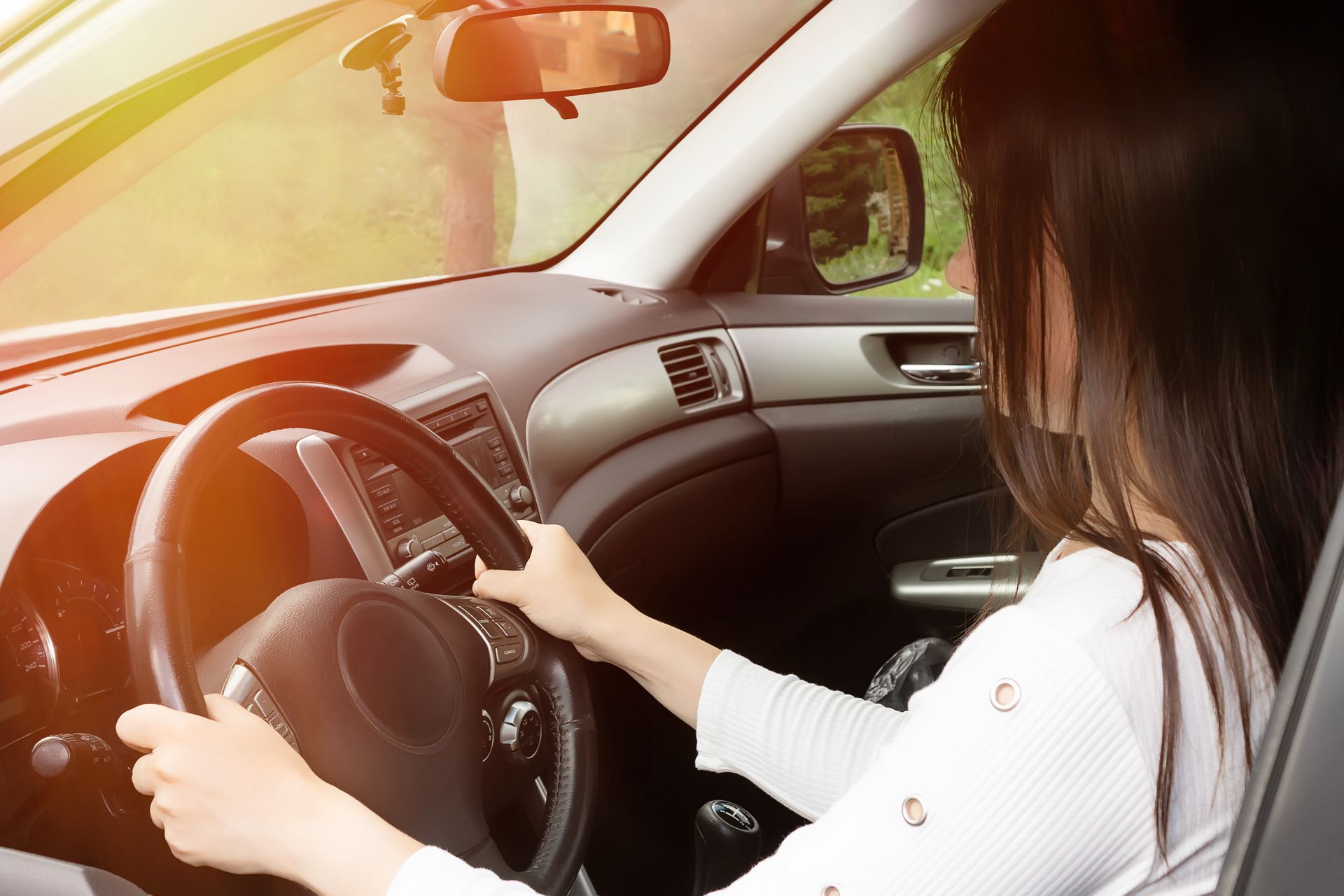 Person driving a car, hands on the steering wheel, with sunlight streaming through the windshield.