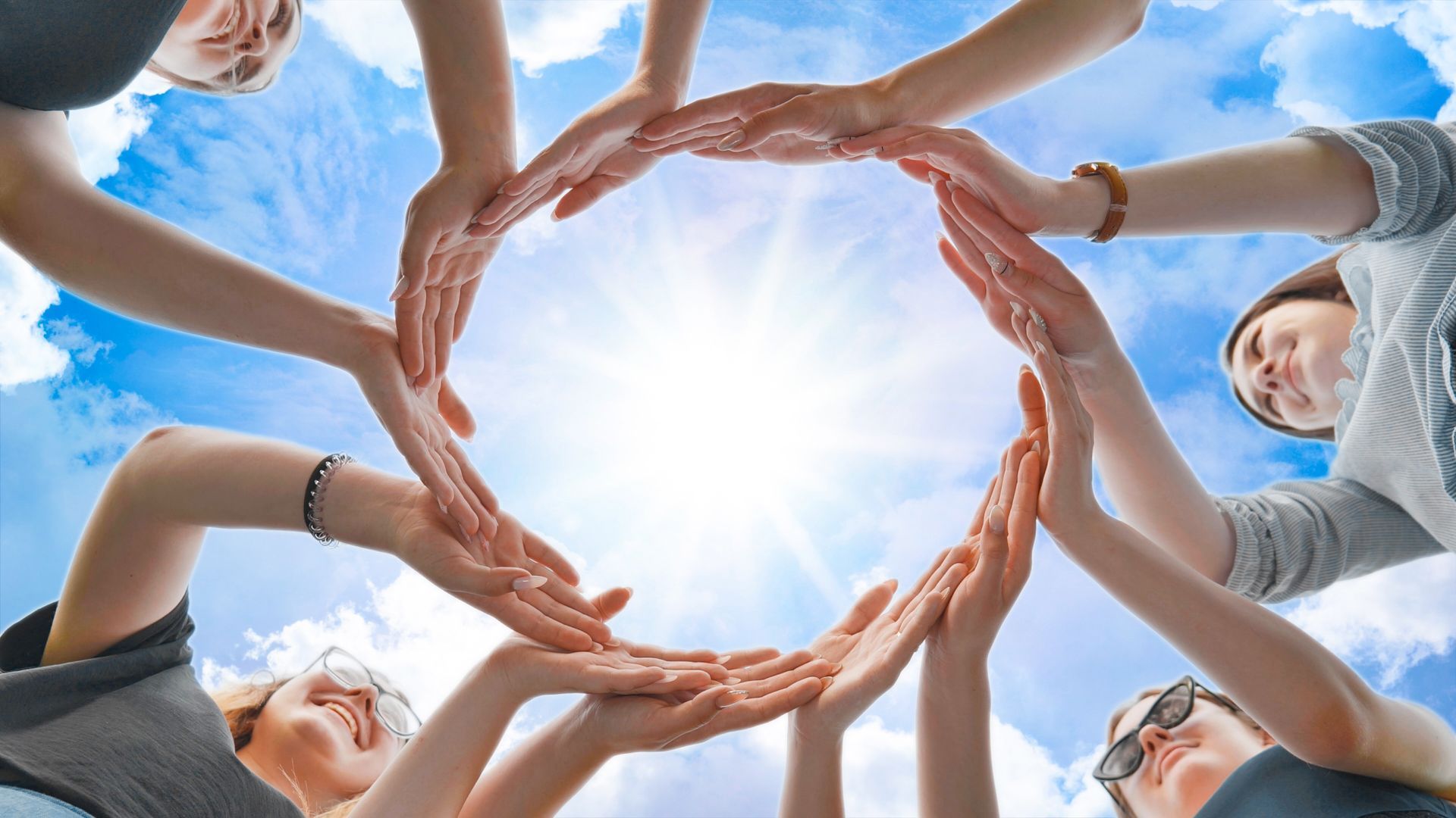 Hands forming a circle against a bright blue sky, symbolizing unity and teamwork
