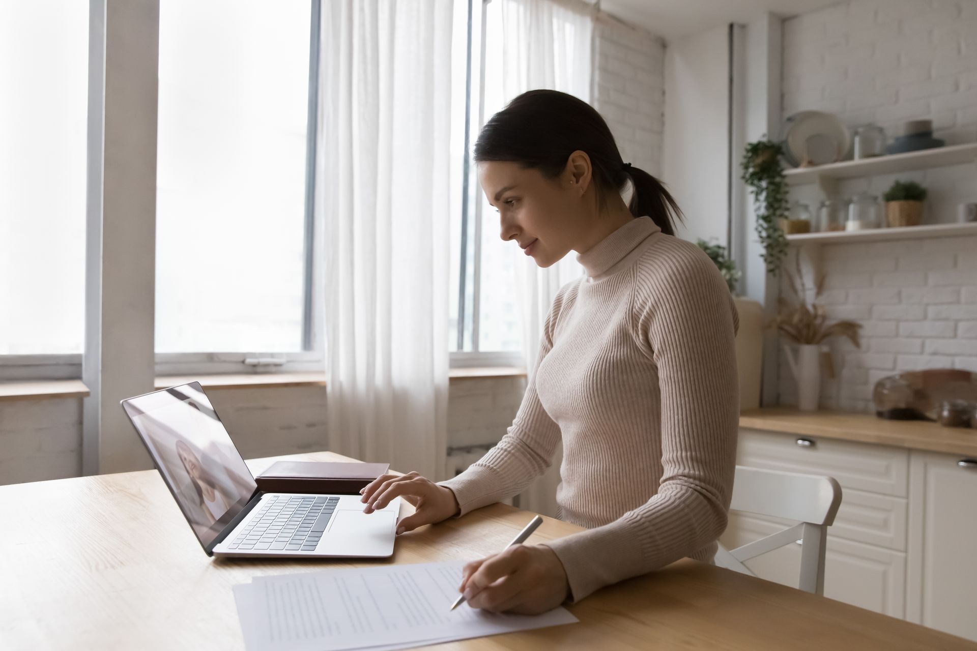 Person working on a laptop at a kitchen table in a bright, white kitchen