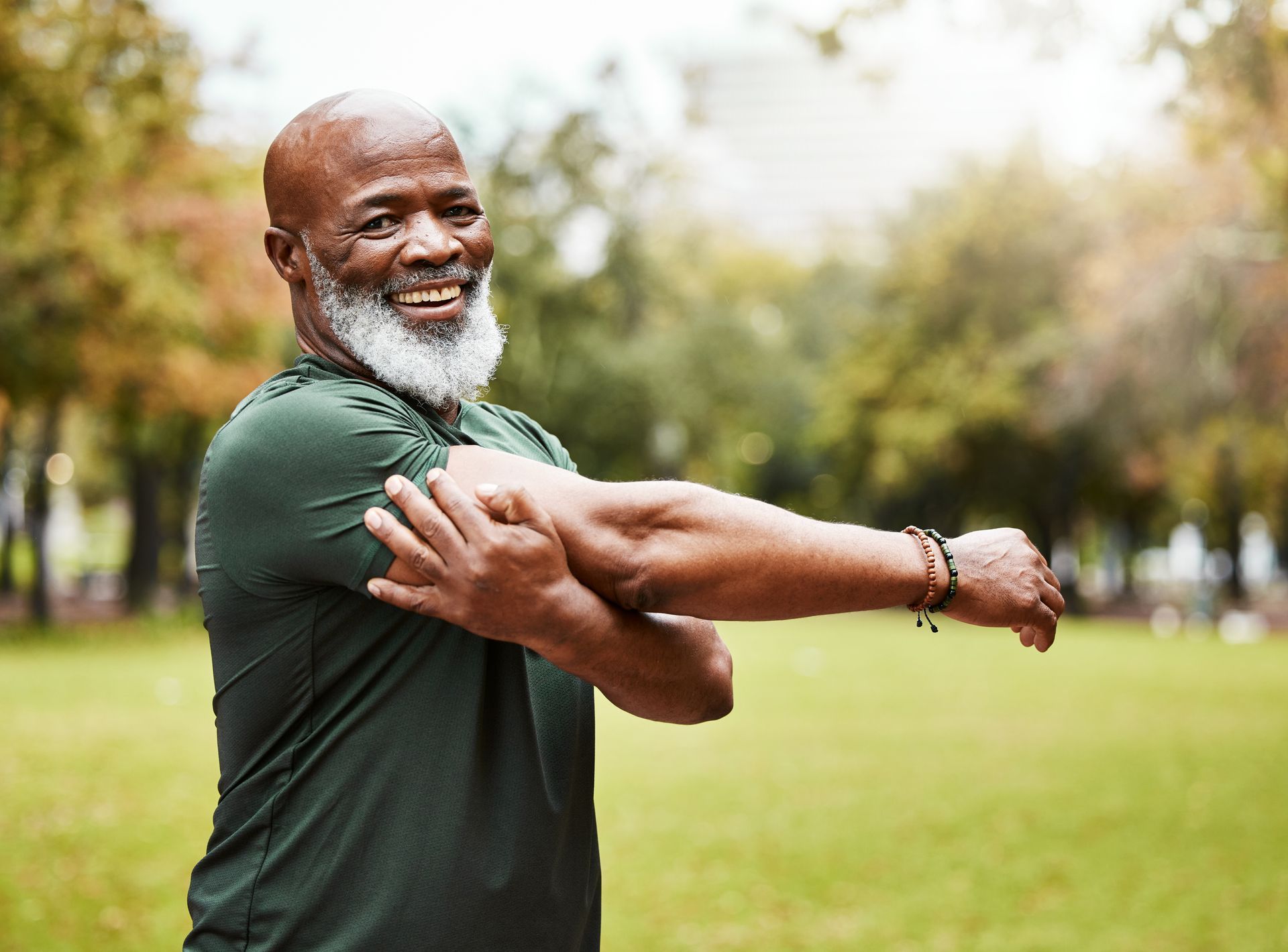 Smiling man in a green shirt stretching his arm in a park