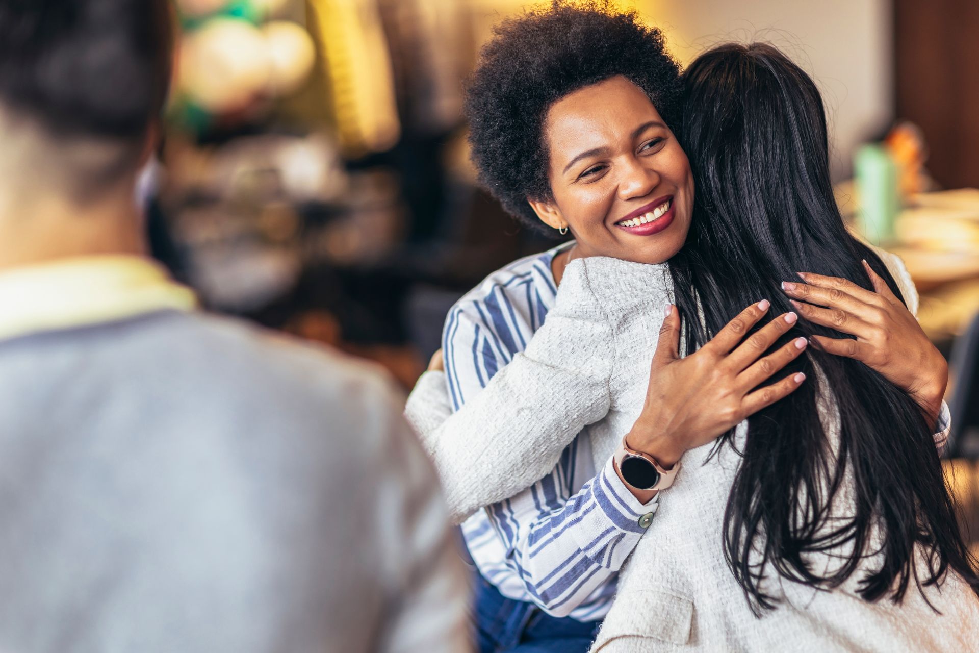 Two people hugging warmly indoors, with one smiling and wearing a striped shirt.