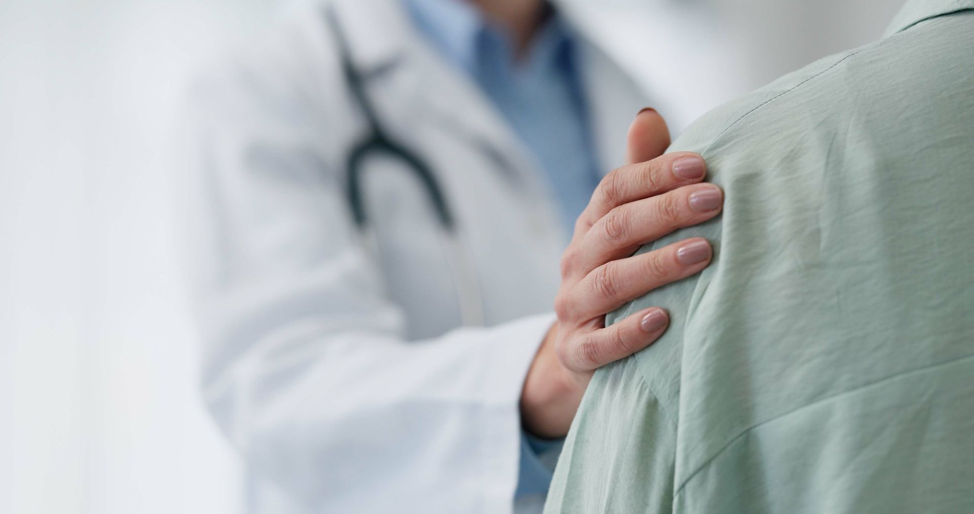 Doctor in white coat places a hand on a patient’s shoulder in a clinical setting