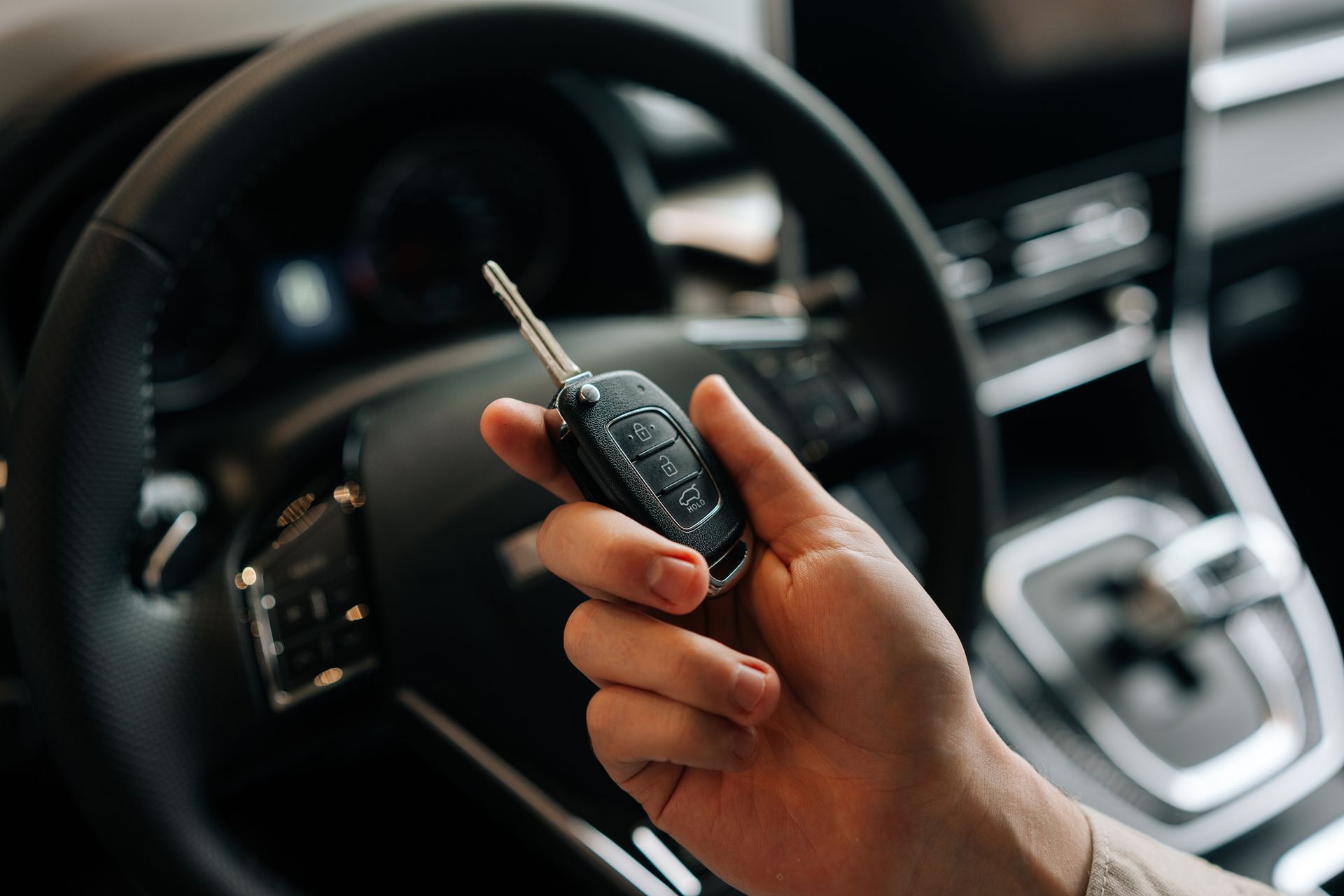 Hand holding a car key fob inside a vehicle, with the steering wheel and dashboard in view