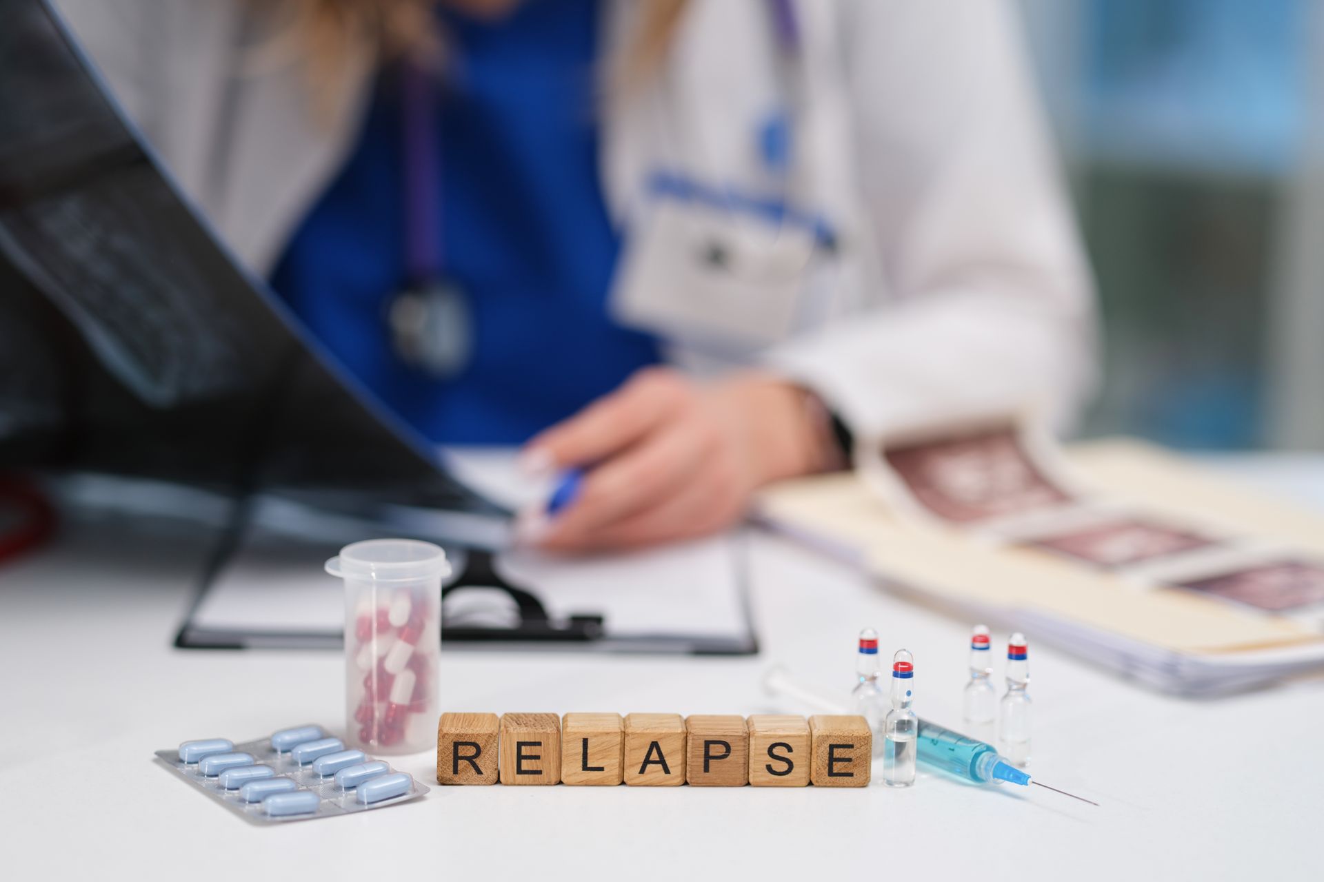 Doctor with medicine and test tubes beside blocks spelling “RELAPSE” on a desk